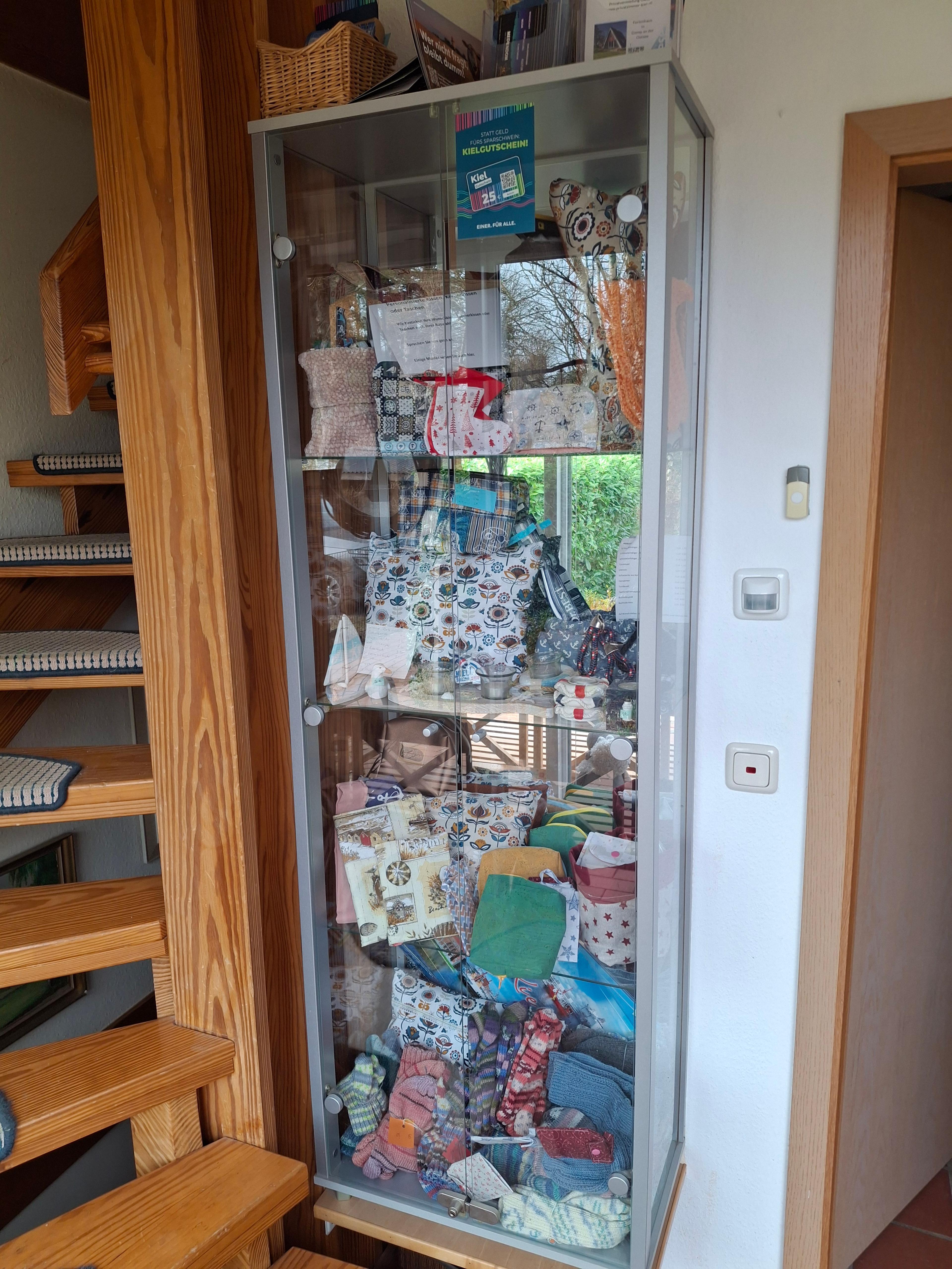 Glasvitrine mit bunten, handgemachten Stoffwaren und Accessoires im Flur neben Holztreppe