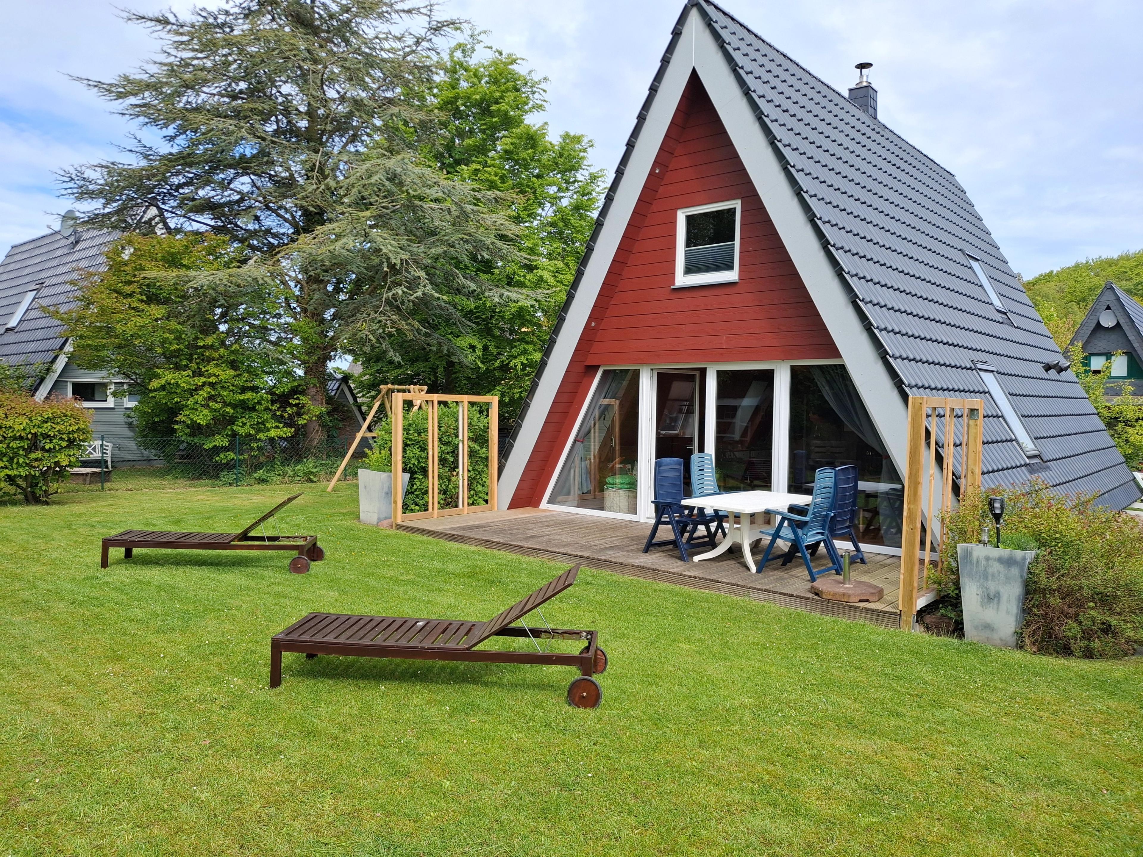 A-Frame-Haus mit rotem Holz, grüner Garten mit Liegestühlen und Baumschaukel