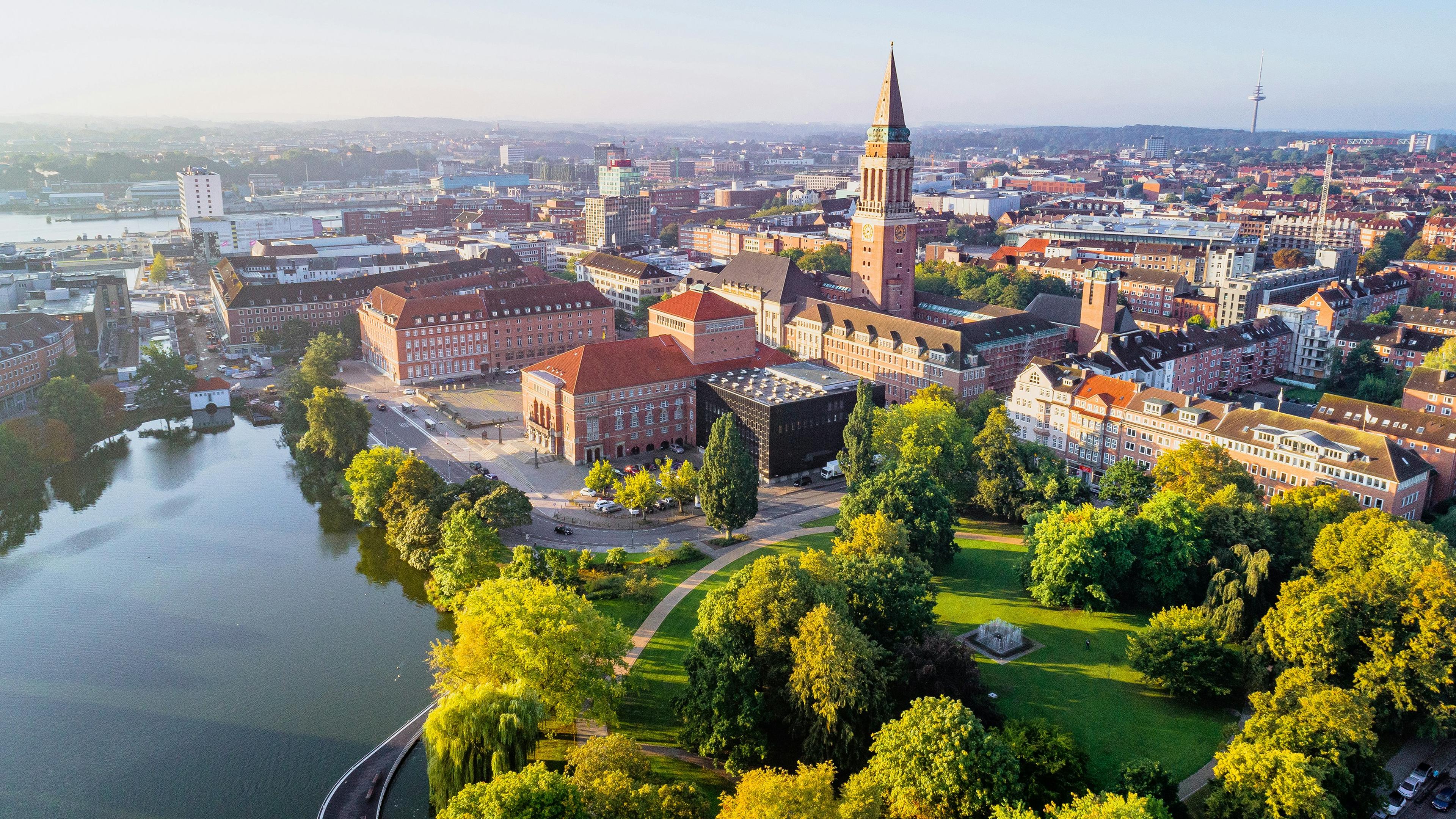 Rotes Backstein-Rathaus von Kiel mit hohem Turm, spiegelt sich im See