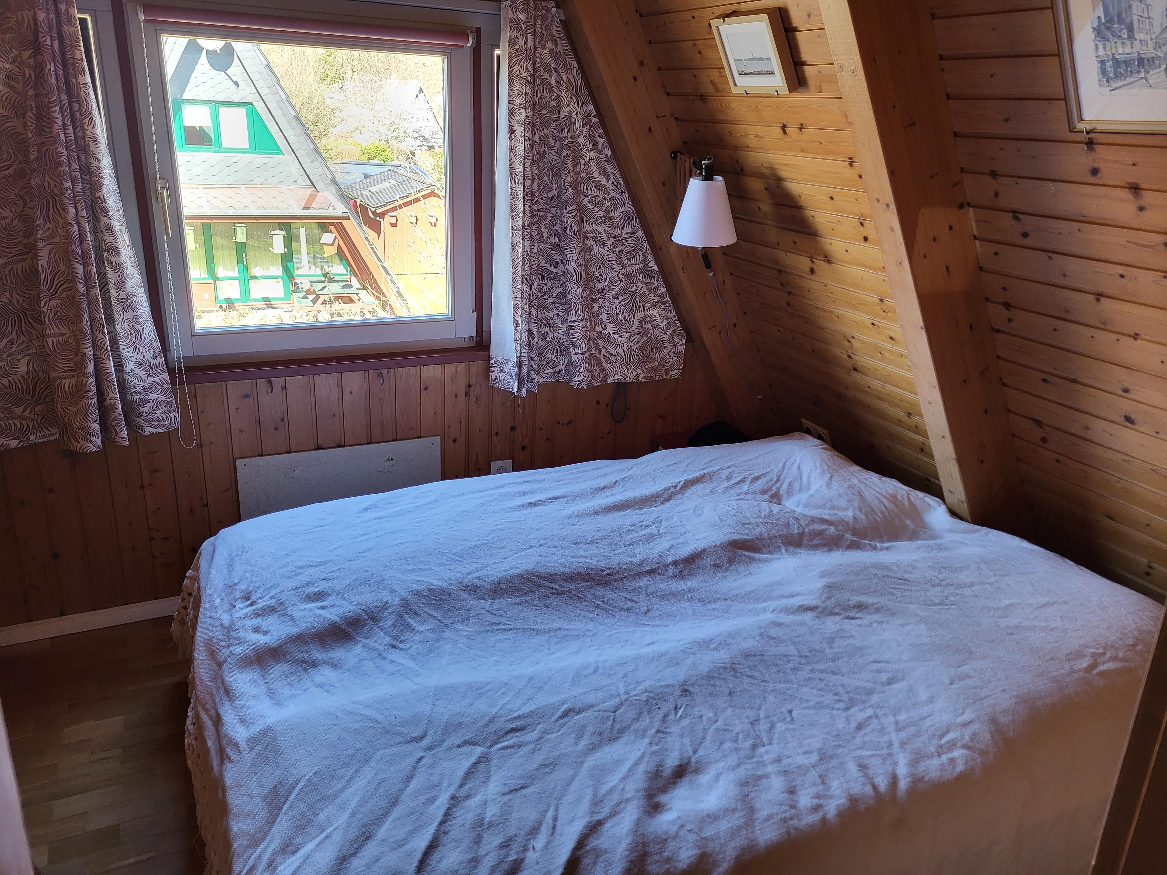 Dachzimmer mit Holzwänden, Bett und Fenster mit Blick nach draußen