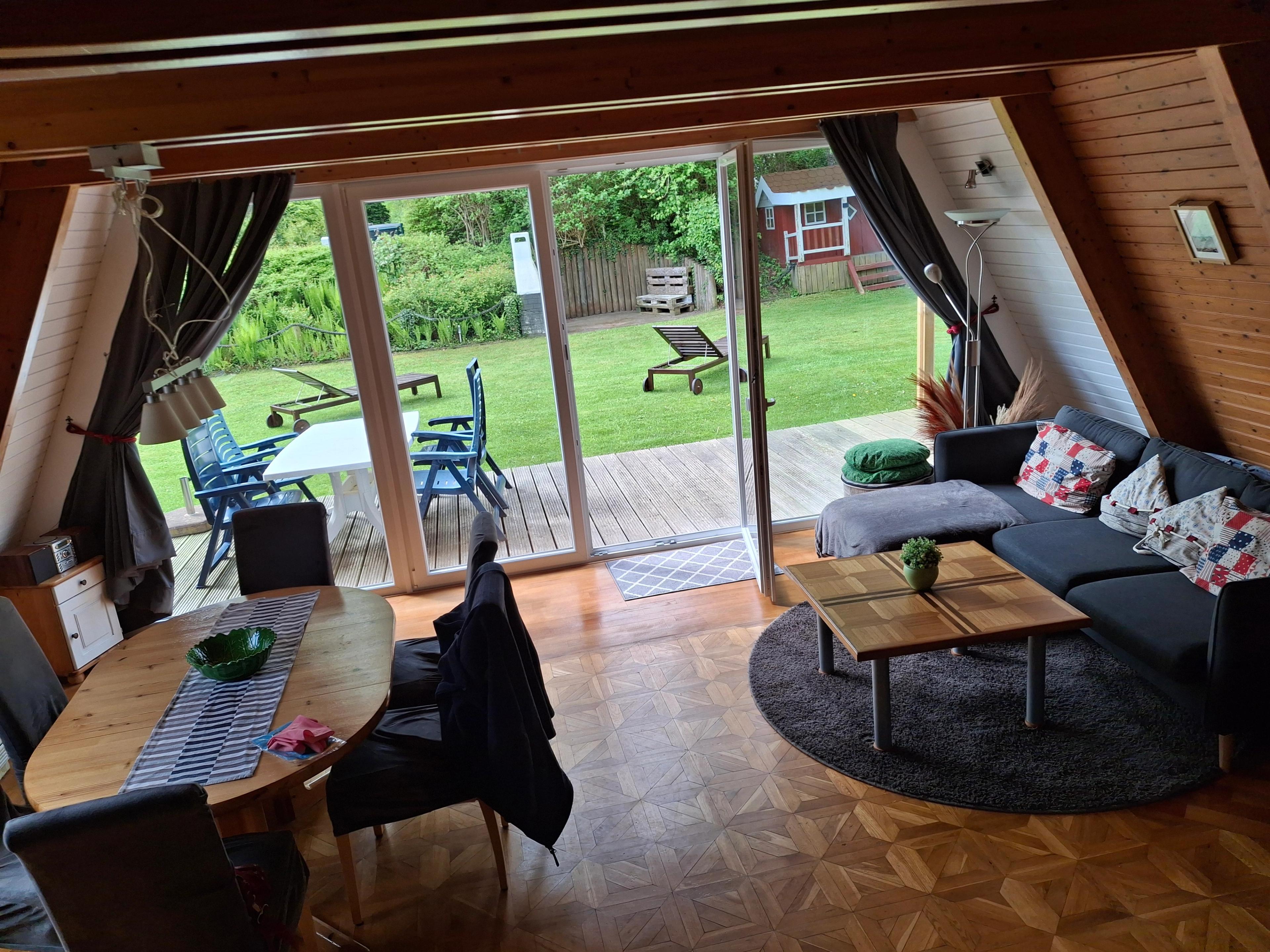 Wohnzimmer mit Holztisch, Sofa, Terrassentür zum Garten, heller Raum