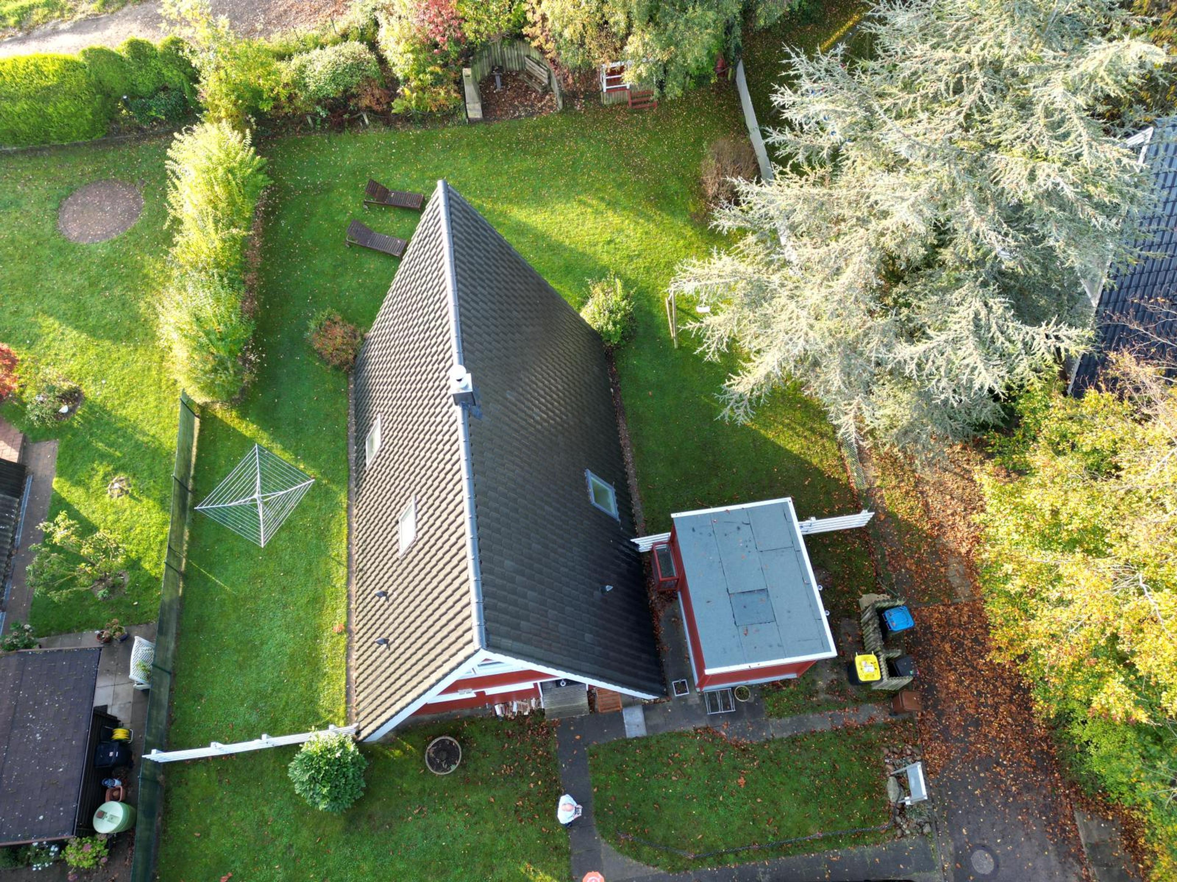 Dach eines Einfamilienhauses in einem Garten mit Bäumen und Wäschespinner von oben