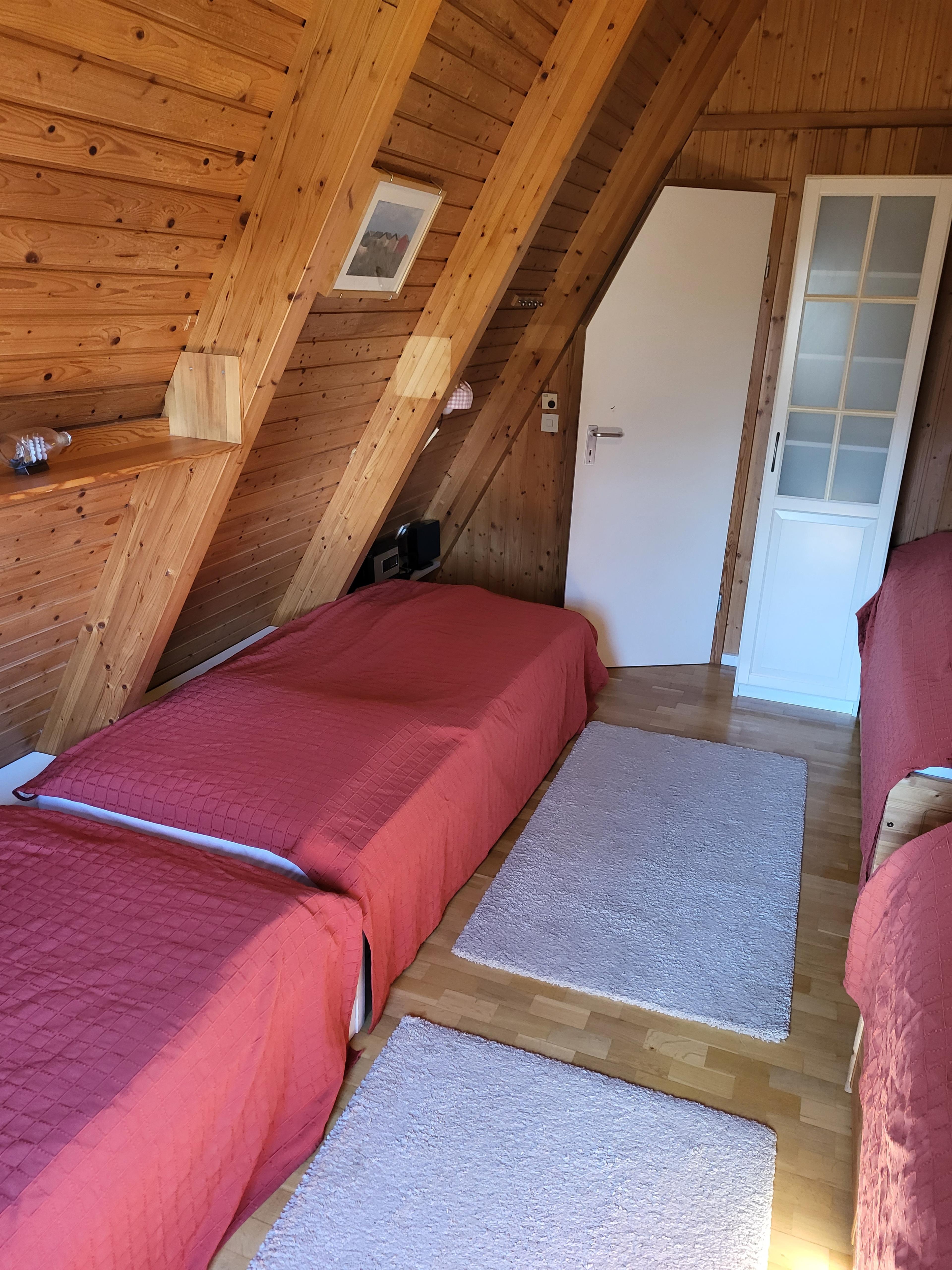 Schlafzimmer im Dachboden mit Holzvertäfelung, roten Decken und Teppichen