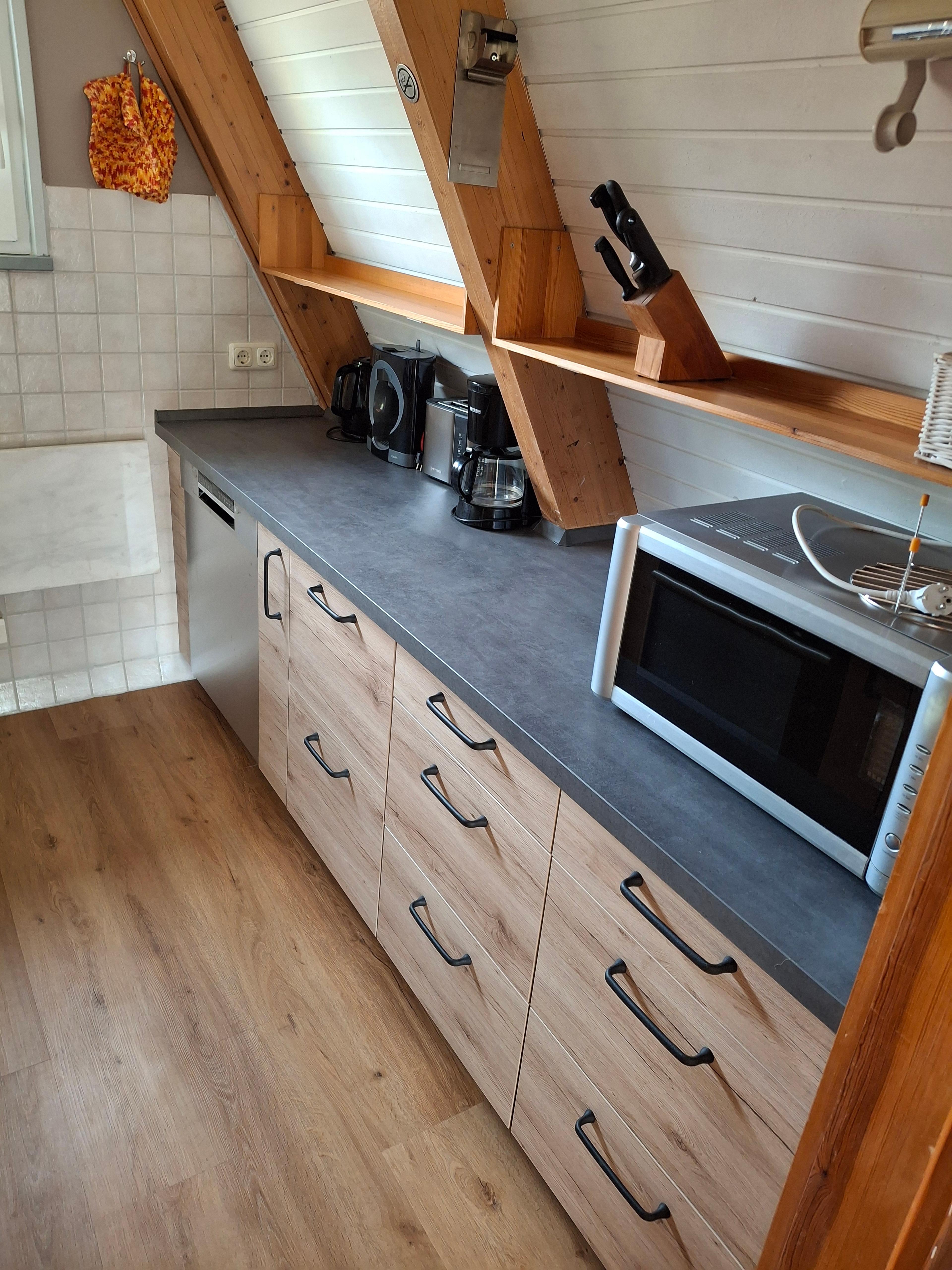 Neue Küchenarbeitsplatte mit Holzschränken, Geräten, Messerblock und Mikrowelle in hellem, modernem Raum.