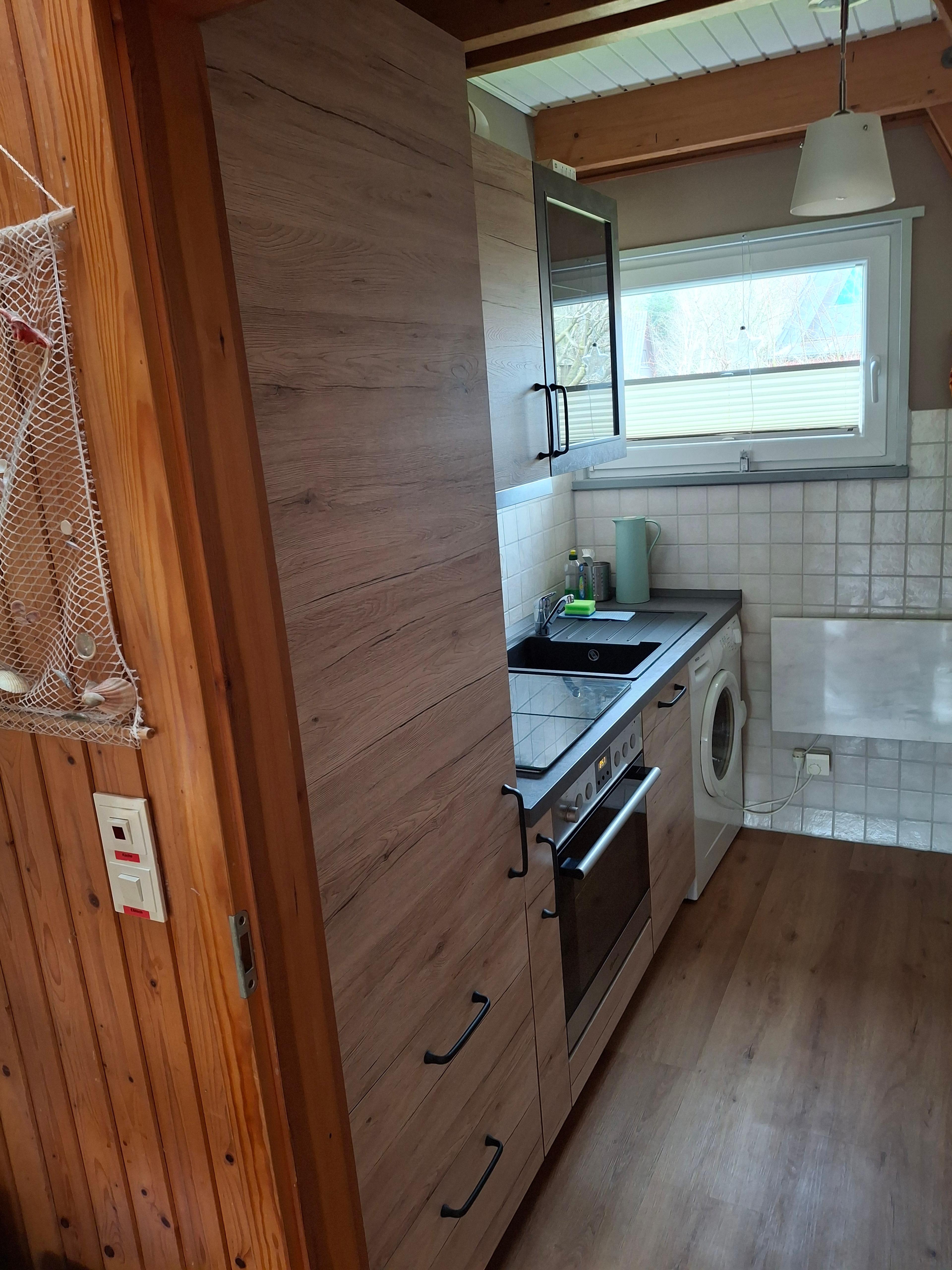 Neue Einbauküche mit Holzschränken, Herd, Waschmaschine und Fenster