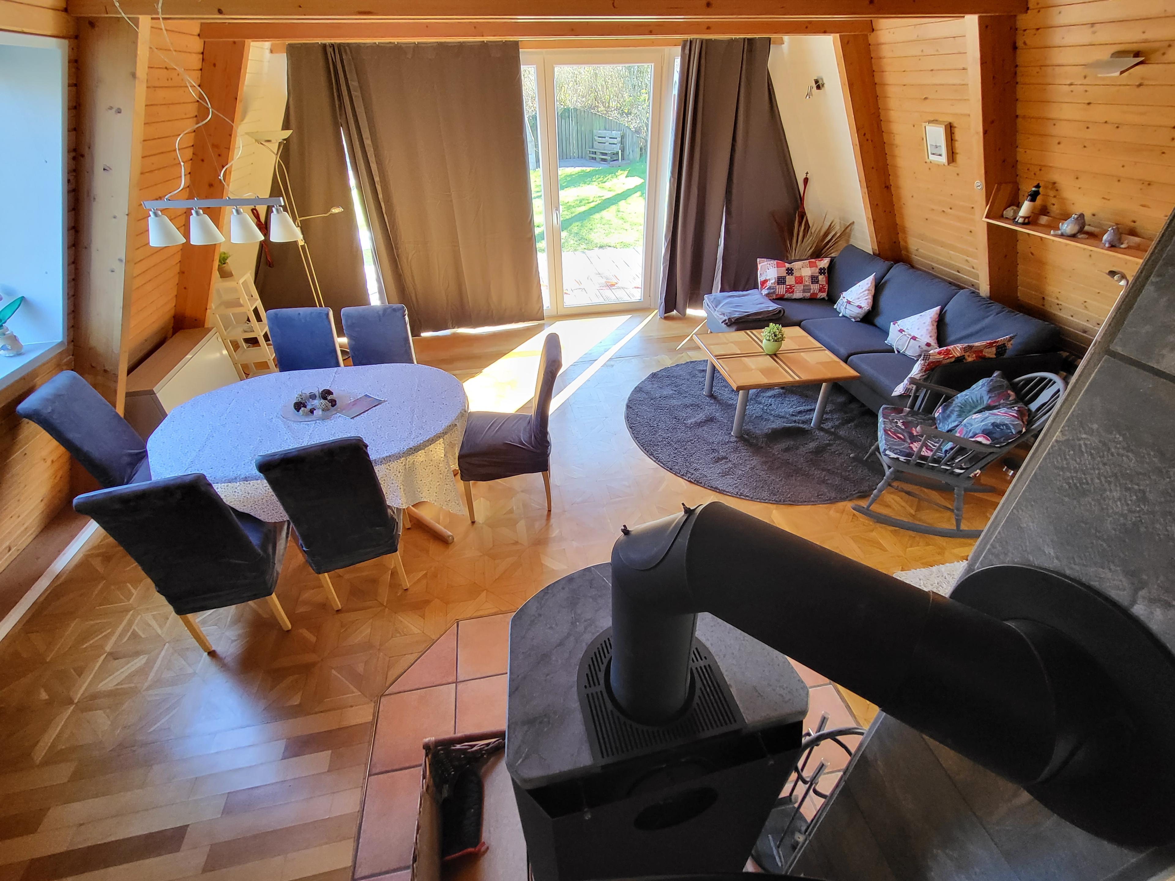 Wohnzimmer mit Kamin, Esstisch, Sofa und großen Fenstern mit Blick in den Garten.