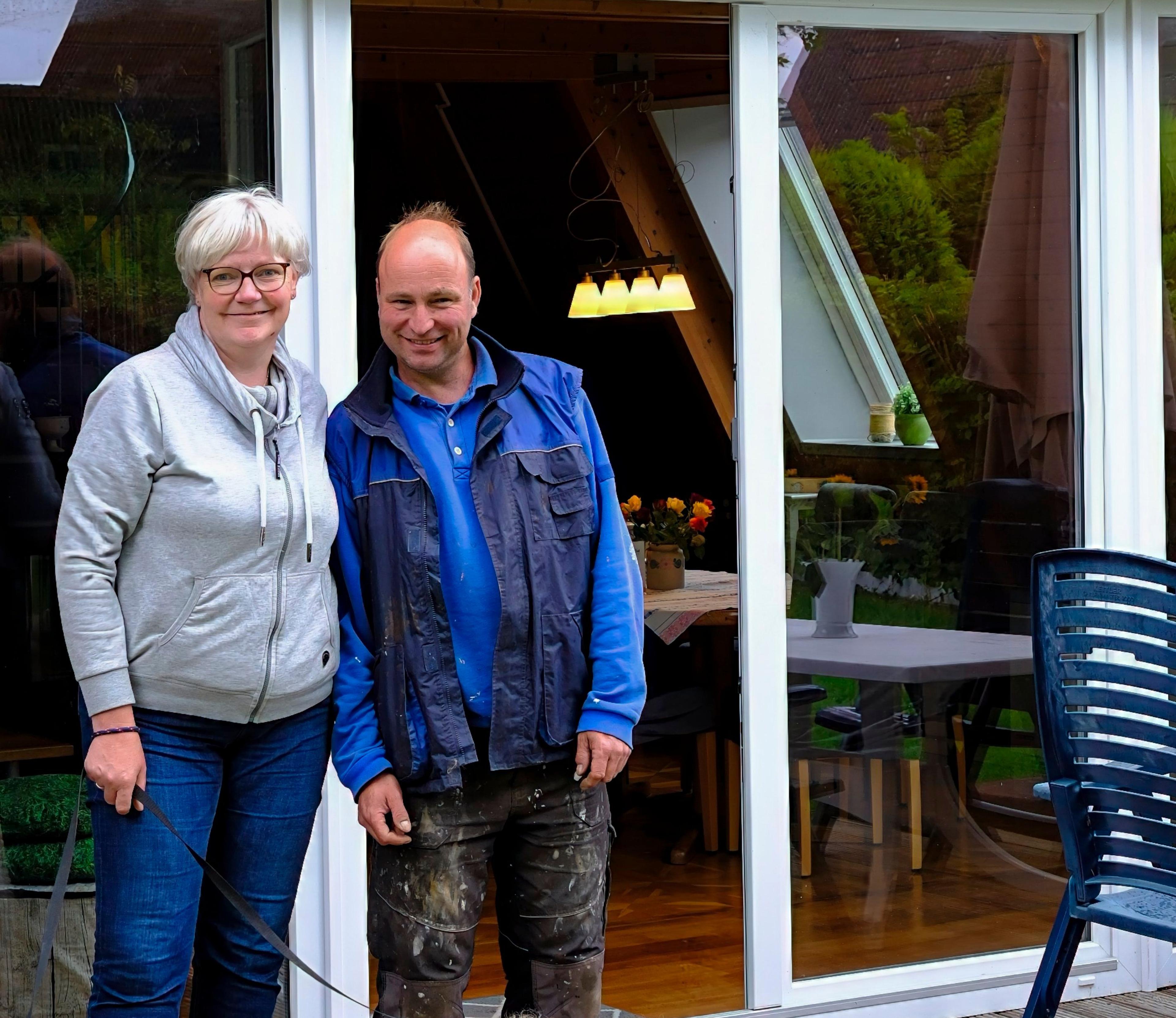Die Gastgeber stehen auf der Terrasse; im Hintergrund ein Haus mit Glasfront.