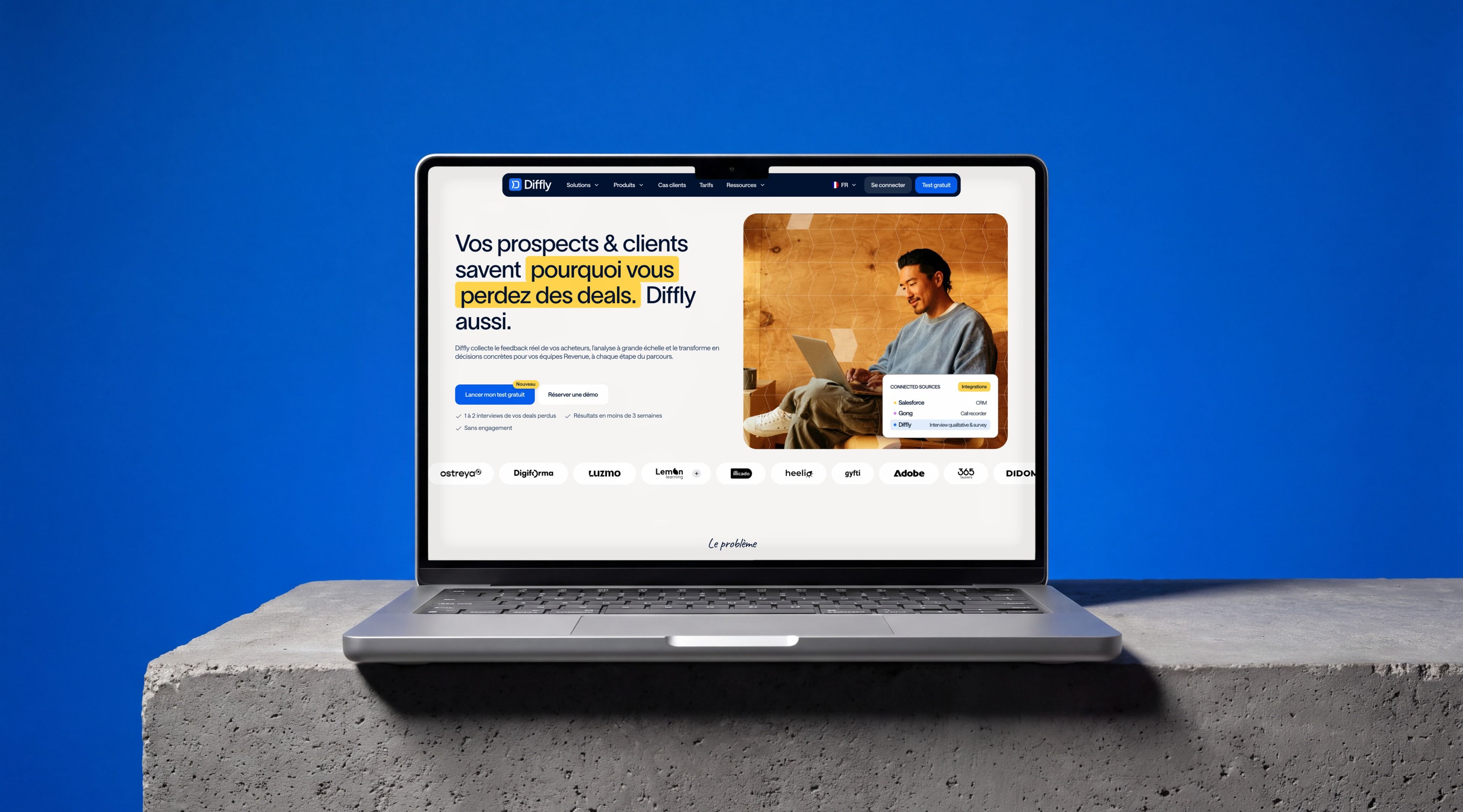 MacBook Pro on a concrete block against a blue backdrop, showing the Diffly home page “Your prospects & customers know why you lose deals”