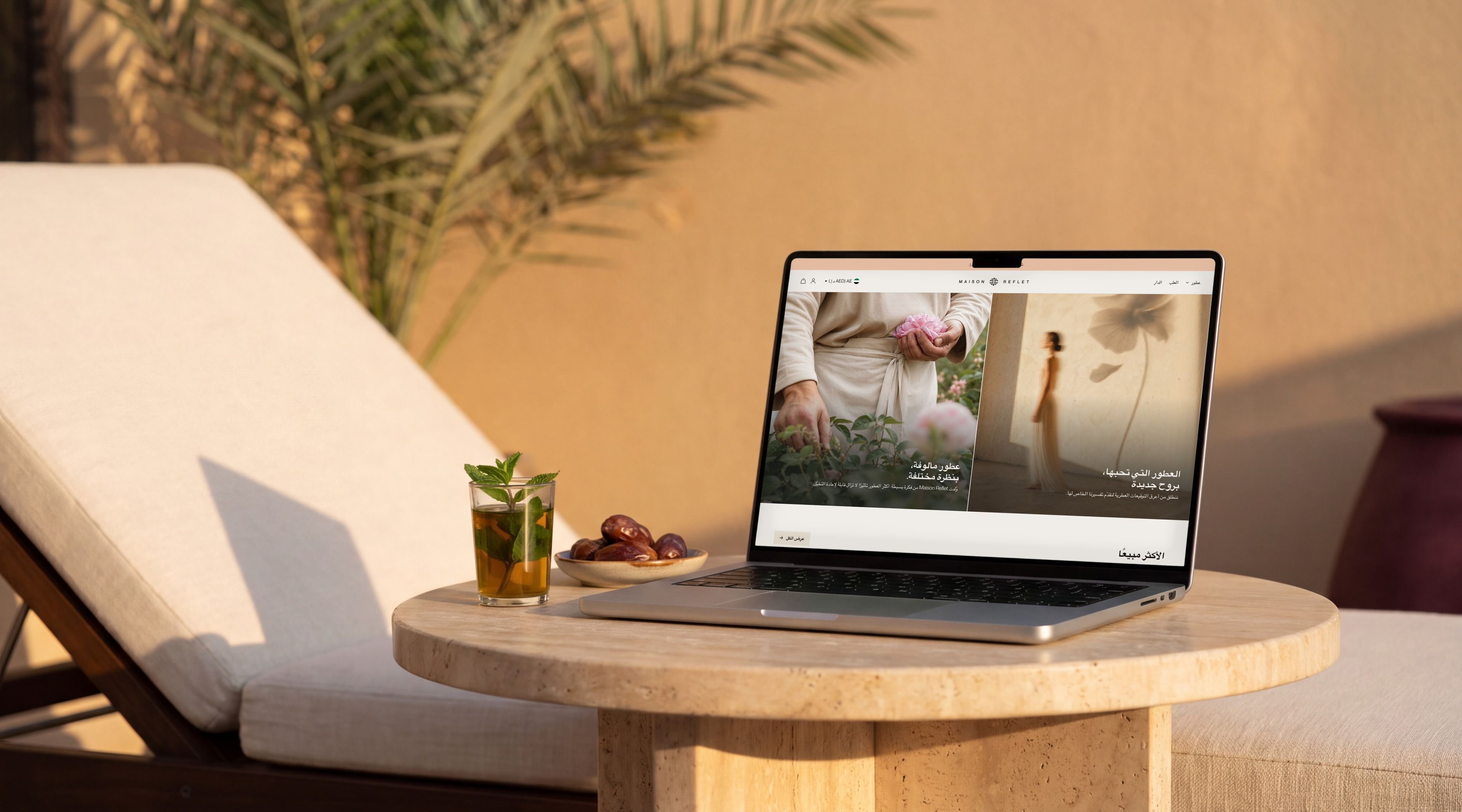 MacBook Pro open on the Maison Reflet home page in Arabic, on a terrace at sunset