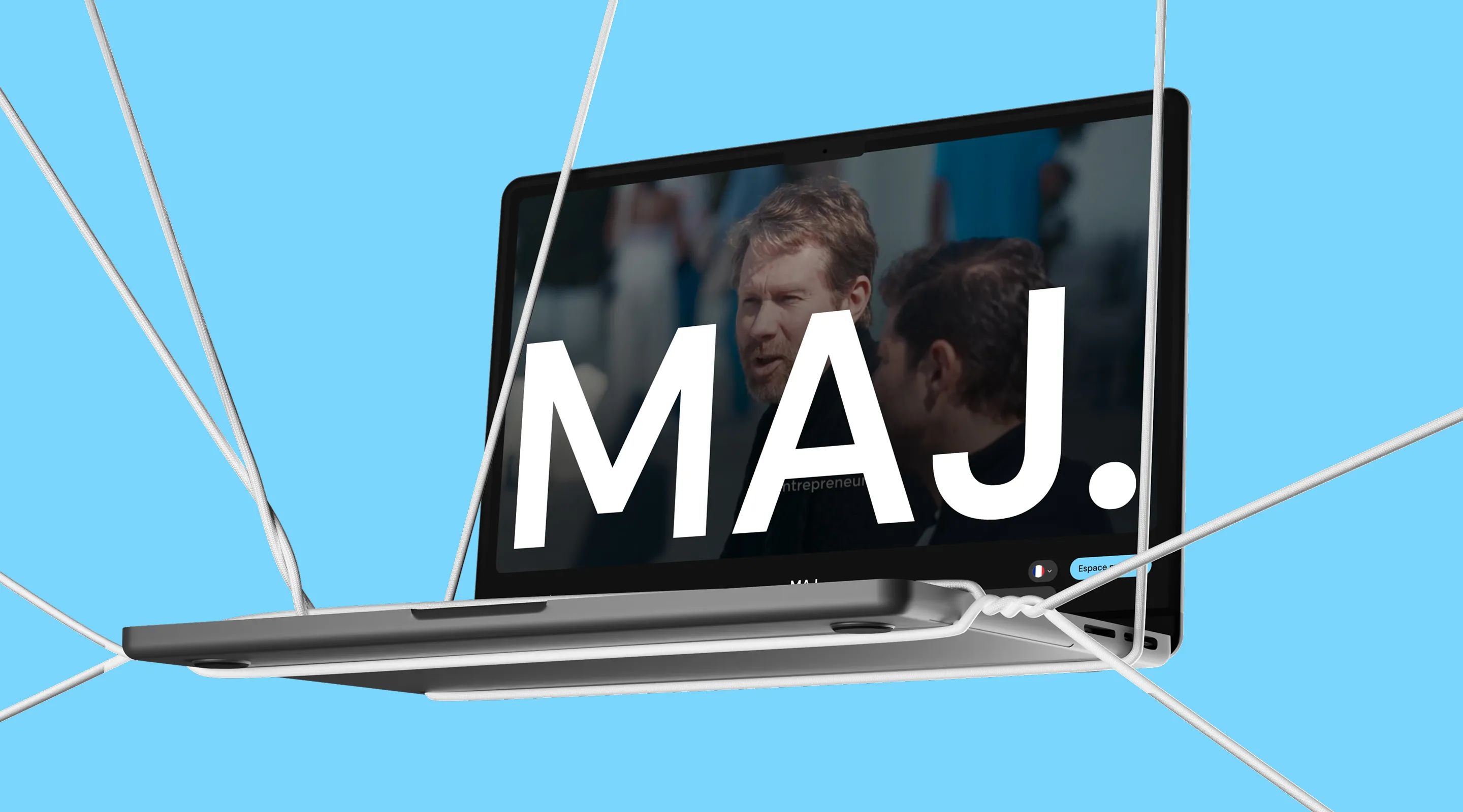 Laptop suspended by cables on a blue background, showing the MAJ website with a large “MAJ.” logo over a video