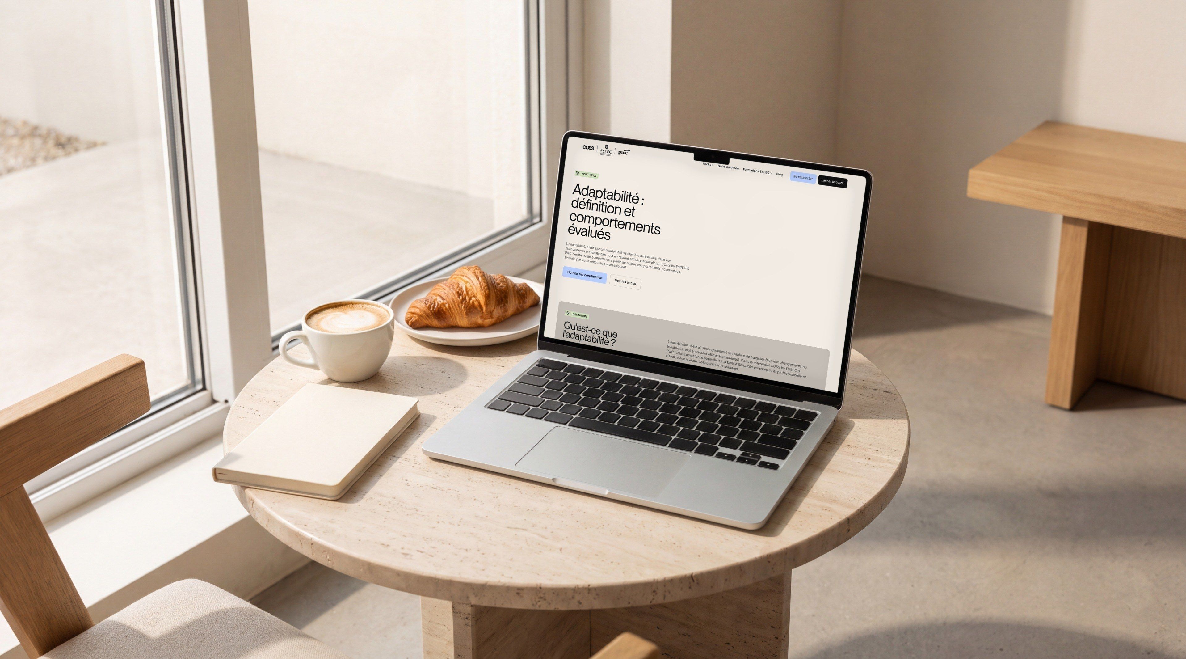 MacBook Pro on a travertine café table, open on the COSS page “Adaptability: definition and assessed behaviours”