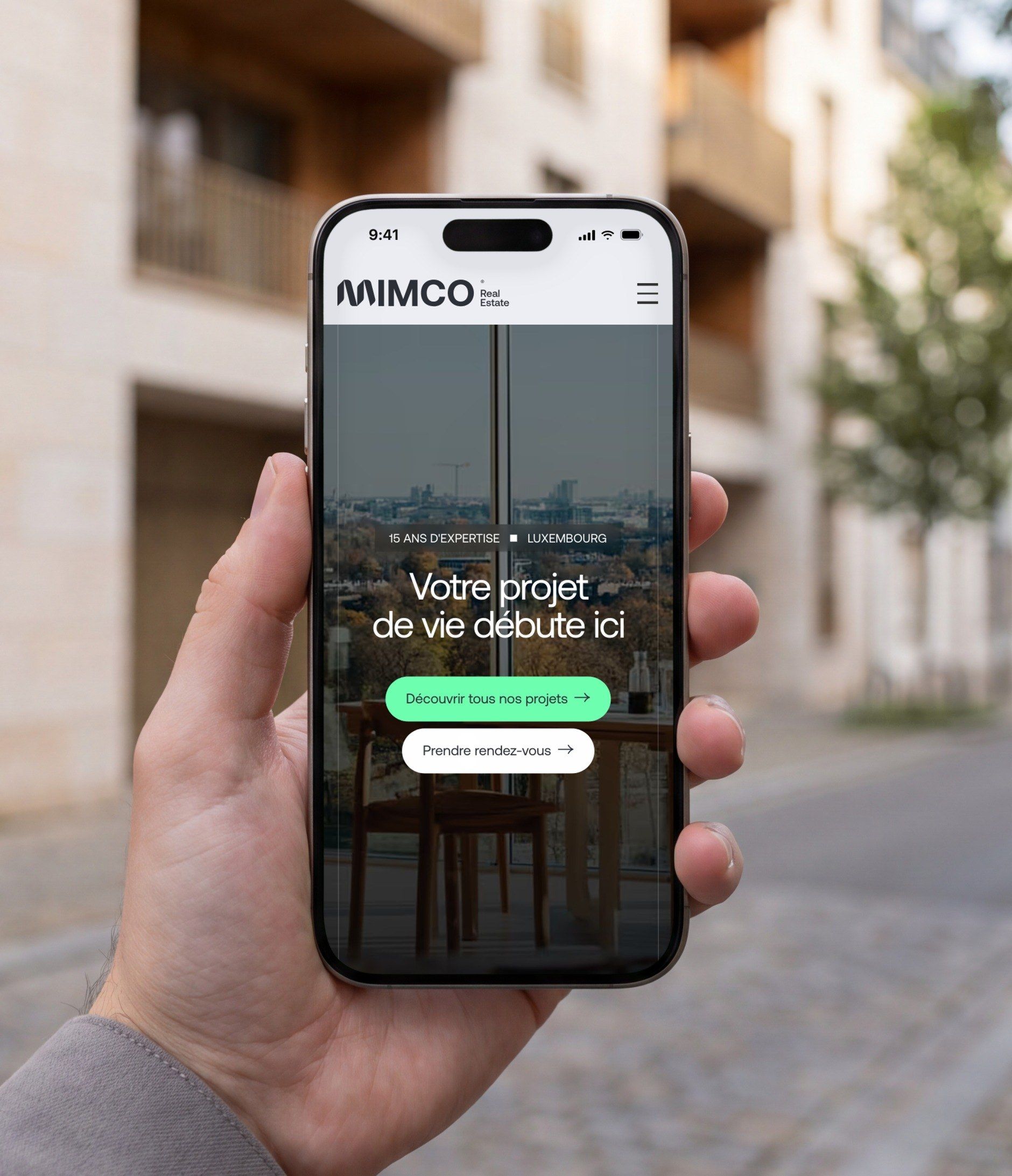 iPhone held in a residential street, open on the Mimco mobile home page