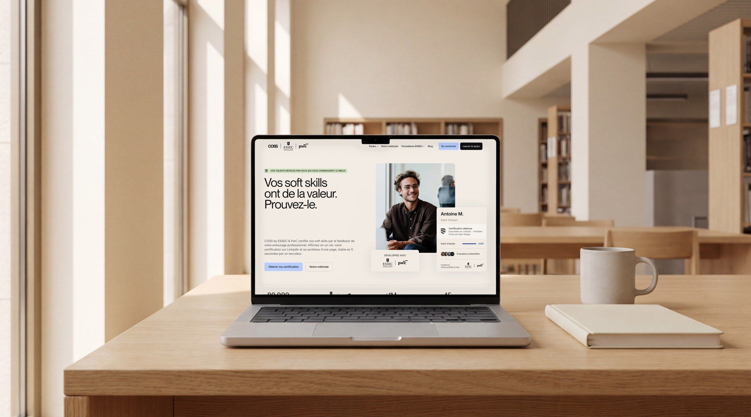 MacBook Pro on an oak desk in a school library, open on the COSS home page, “Your soft skills have value. Prove it.”