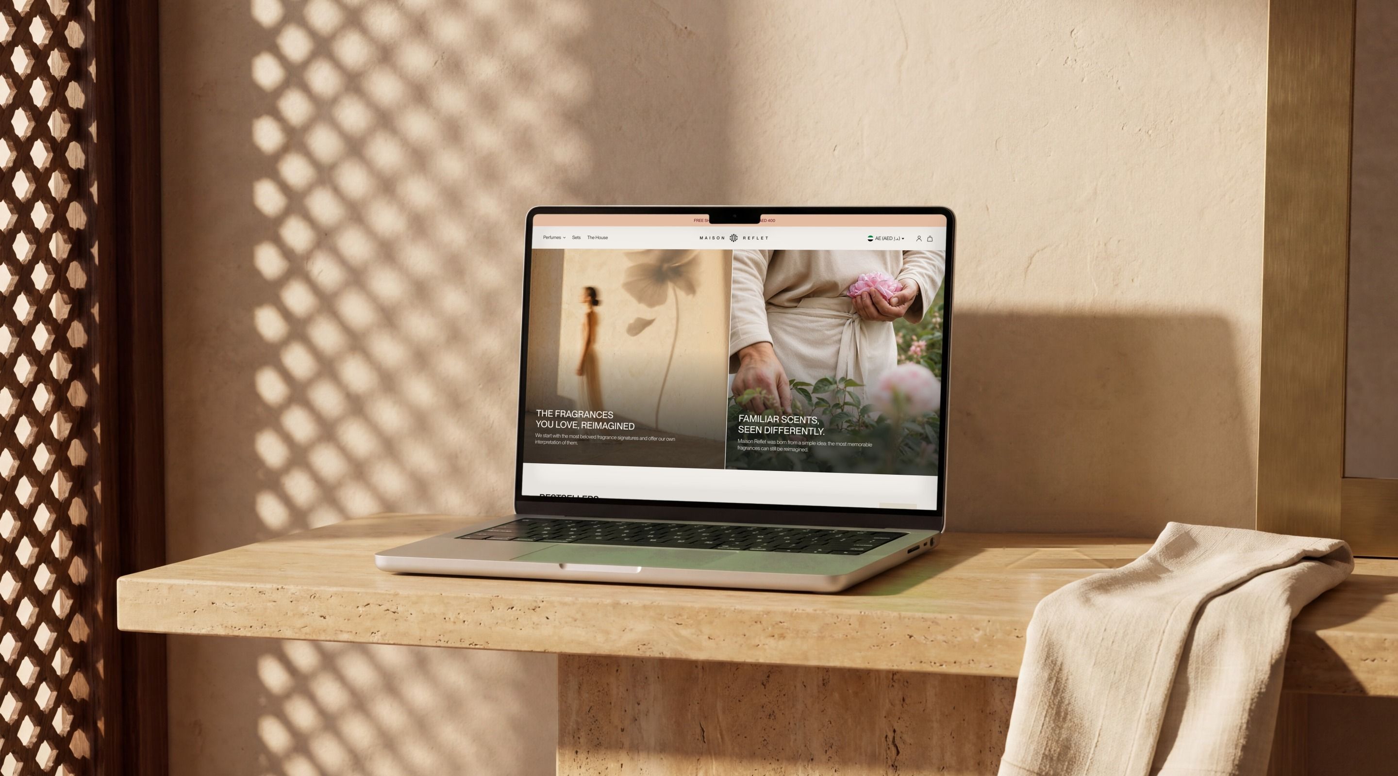MacBook Pro open on the Maison Reflet home page, on a travertine console in the shade of a mashrabiya