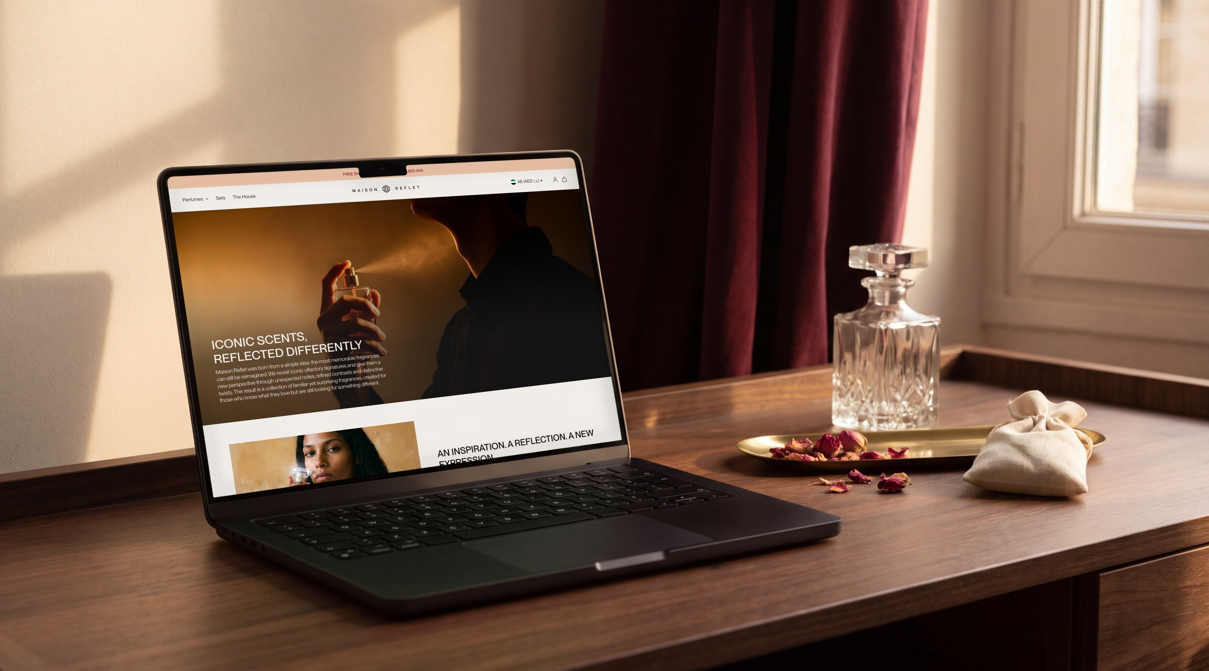 MacBook Pro open on Maison Reflet's The House page, on a walnut dressing table