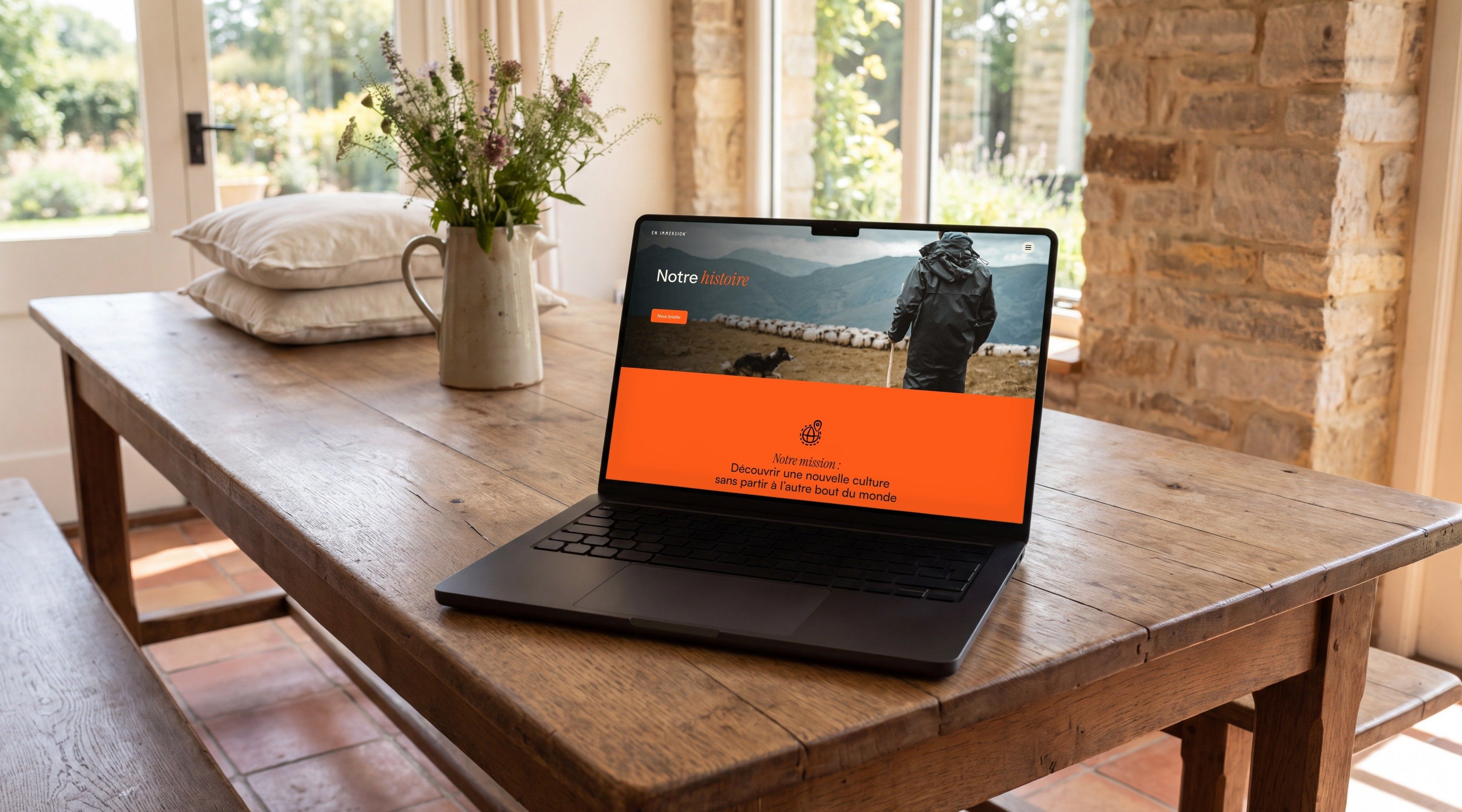 MacBook Pro on a farmhouse table, open on En Immersion's About page, “Our story”