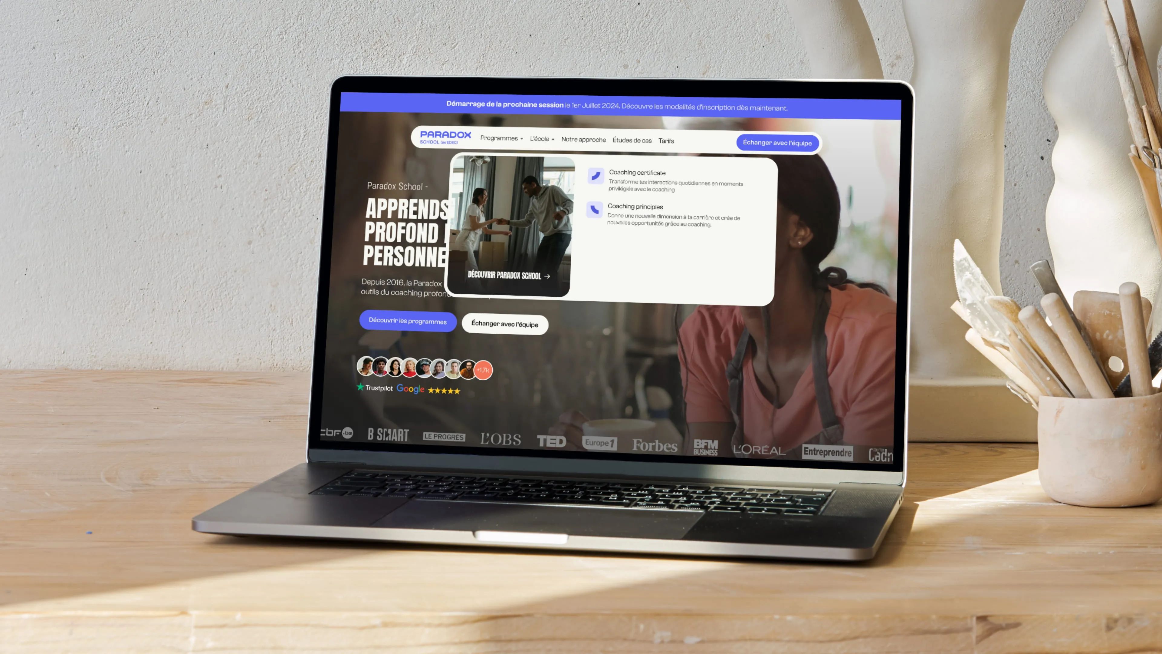Paradox School website on a laptop, Programs menu open showing Coaching certificate and Coaching principles