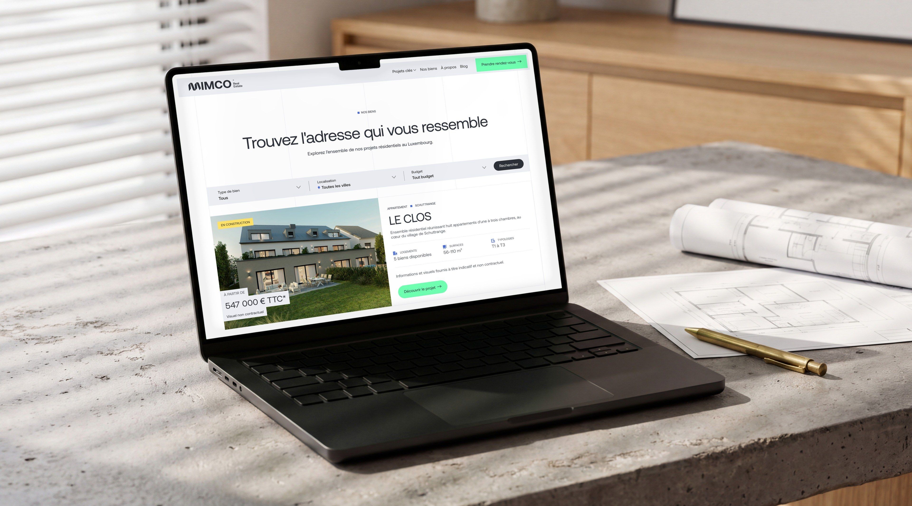 MacBook Pro on a concrete architect's desk with blind shadows, open on the Projects page of the Mimco website
