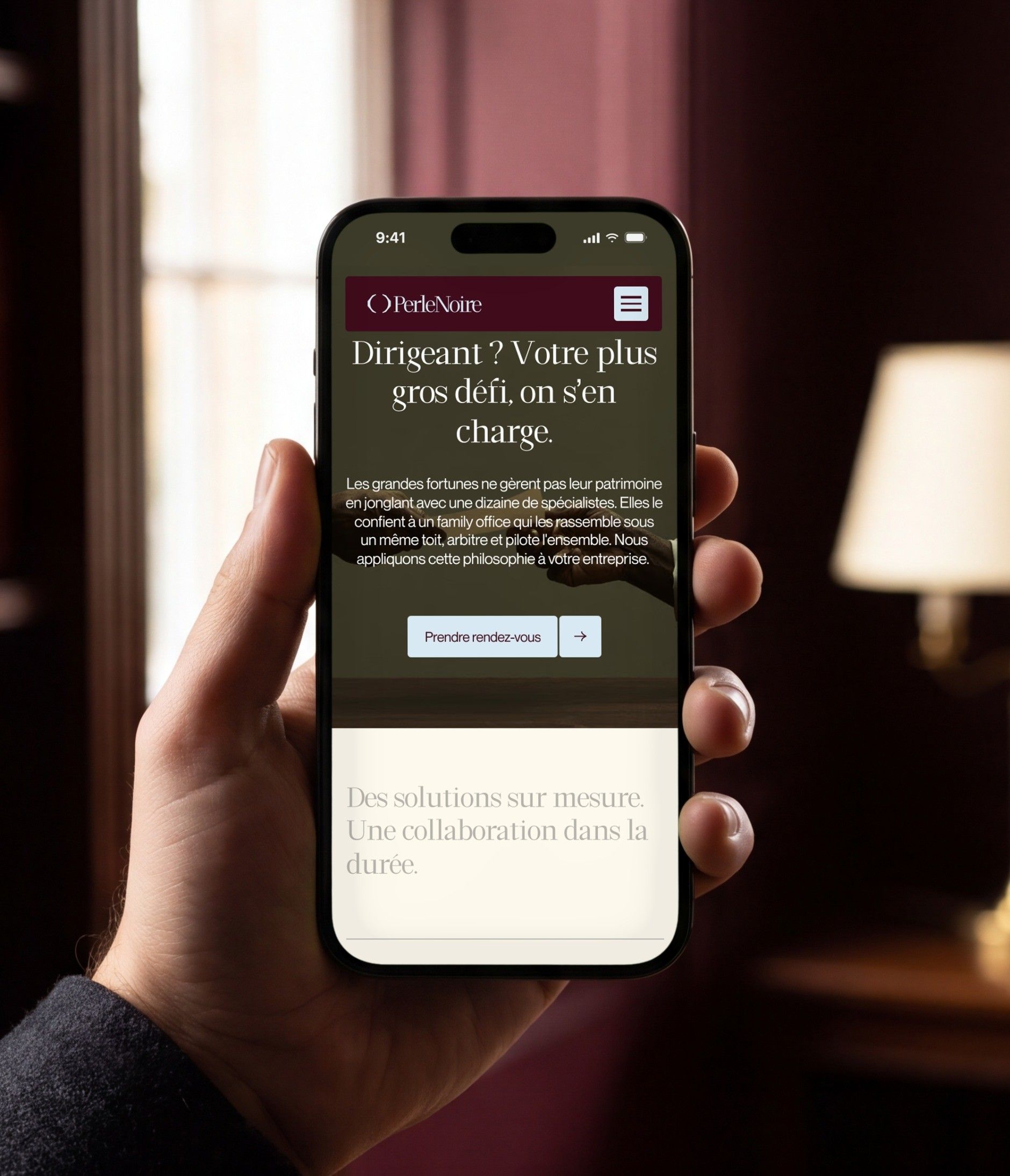 iPhone 16 Pro open on the Perle Noire mobile home page, in a library with burgundy walls