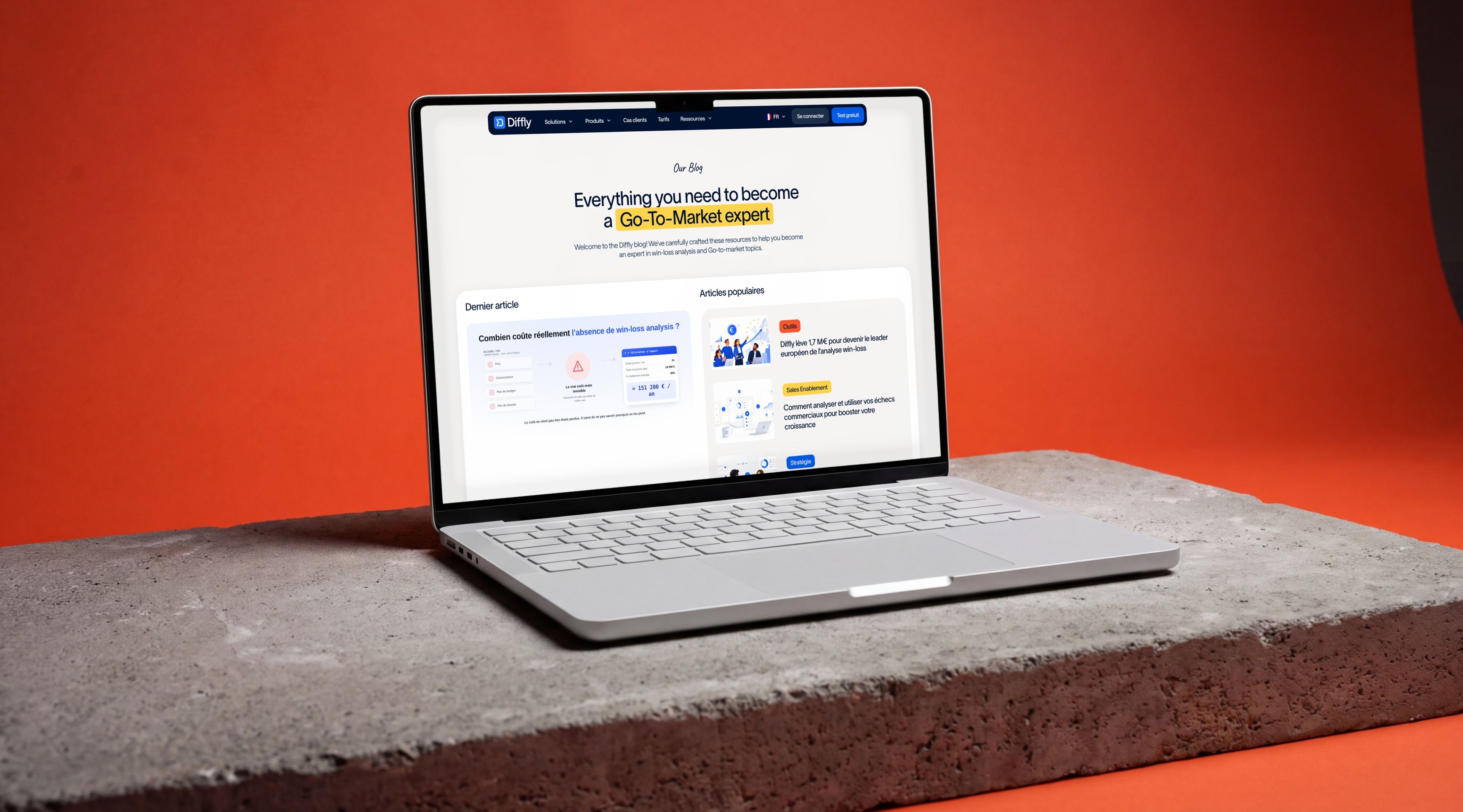 MacBook Pro on a concrete slab against an orange backdrop, showing the Diffly blog hub