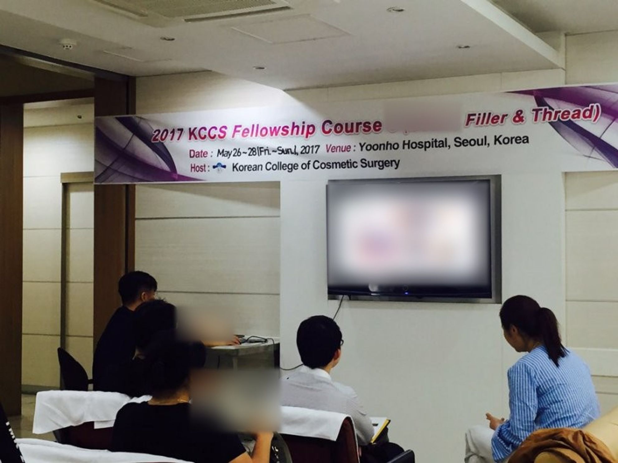 '2017 KCCS Fellowship Course' 현수막 아래 벽걸이 모니터를 향해 참석자들이 앉아 있는 모습(화면 내용과 현수막 일부 글자는 흐리게 처리)