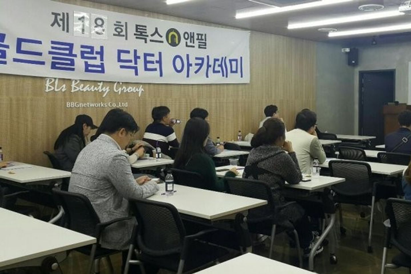 톡스앤필 현수막이 걸린 나무 벽 아래로 참석자들이 책상에 앉아 앞쪽을 바라보는 모습