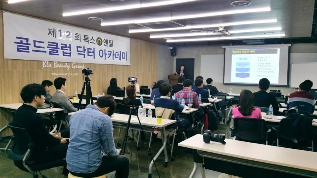 '골드클럽 닥터 아카데미' 현수막이 걸린 강의장에서 참석자들이 책상에 앉아 앞쪽 화면과 마이크를 든 사람을 바라보는 뒷모습