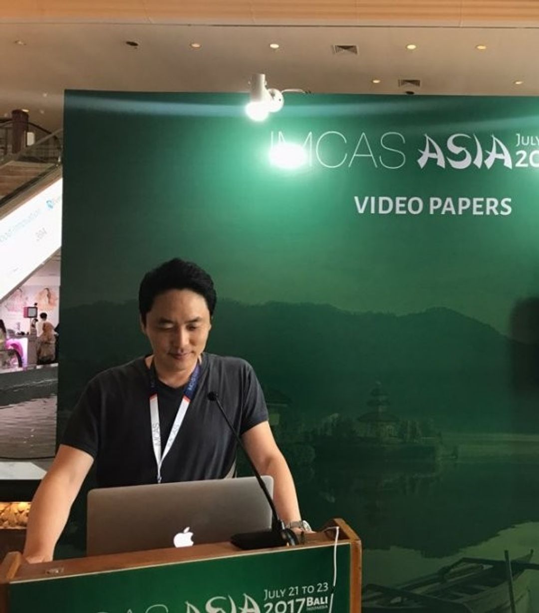 'IMCAS ASIA'와 'VIDEO PAPERS' 글자가 적힌 녹색 배경막 앞 강연대에서 한 사람이 노트북을 보고 있는 모습