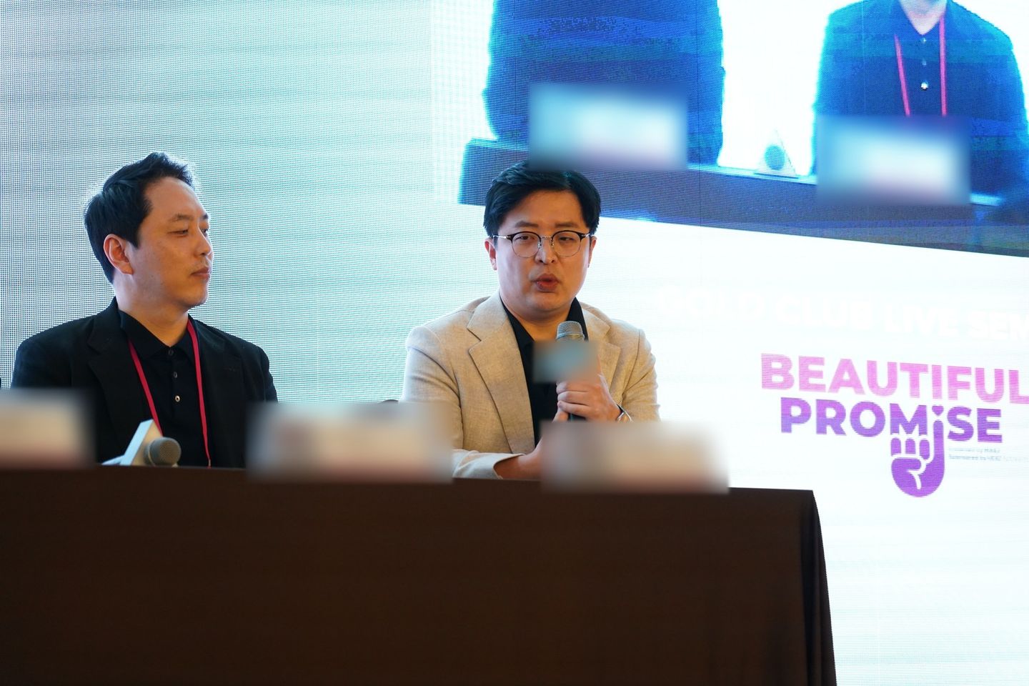 'BEAUTIFUL PROMISE'가 띄워진 무대 화면 앞 패널석에서 한 연자가 마이크를 들고 말하고, 왼쪽 연자가 듣고 있다