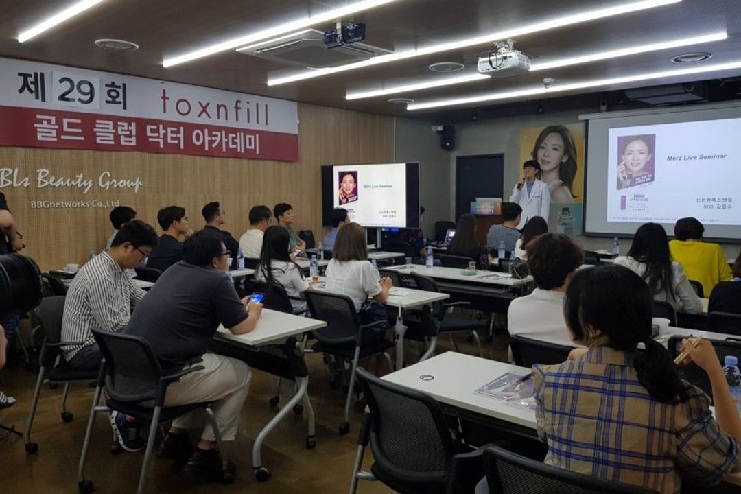 골드클럽 닥터아카데미 현수막이 걸린 강의장에서 흰 가운을 입은 연자가 마이크를 들고 발표하고 참석자들이 앉아 듣는 모습