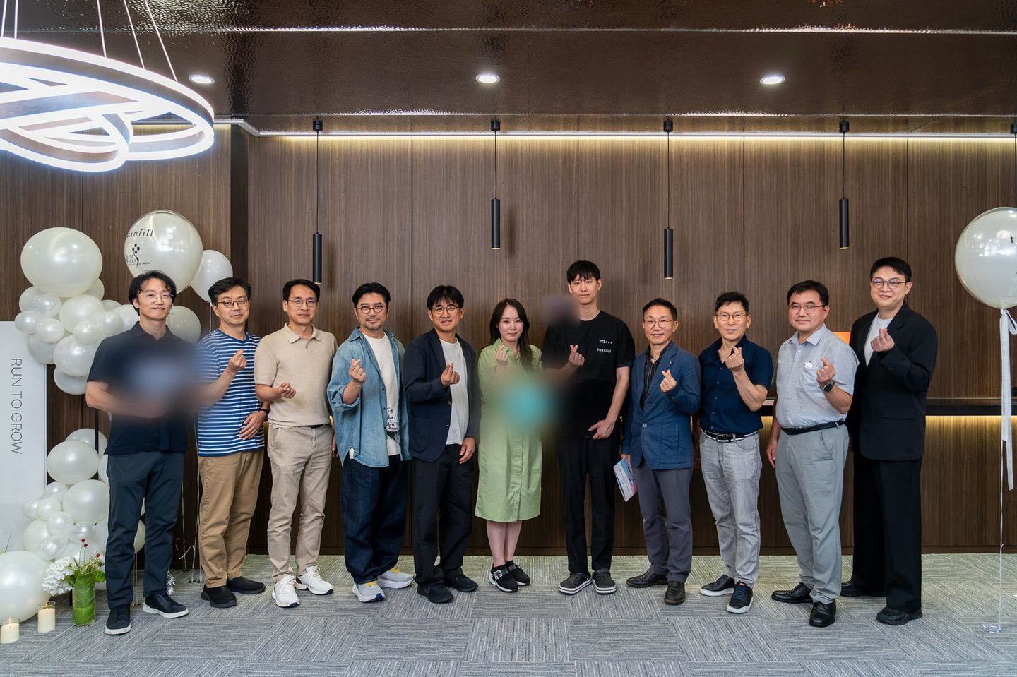 'RUN TO GROW' 배너와 흰 풍선 장식 앞에서 참석자 열두 명이 나란히 서서 사진을 찍고 있다