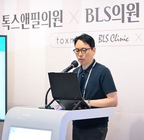 '톡스앤필의원 × BLS의원' 현수막 앞 강연대에서 한 사람이 노트북을 보며 마이크에 대고 말하는 모습