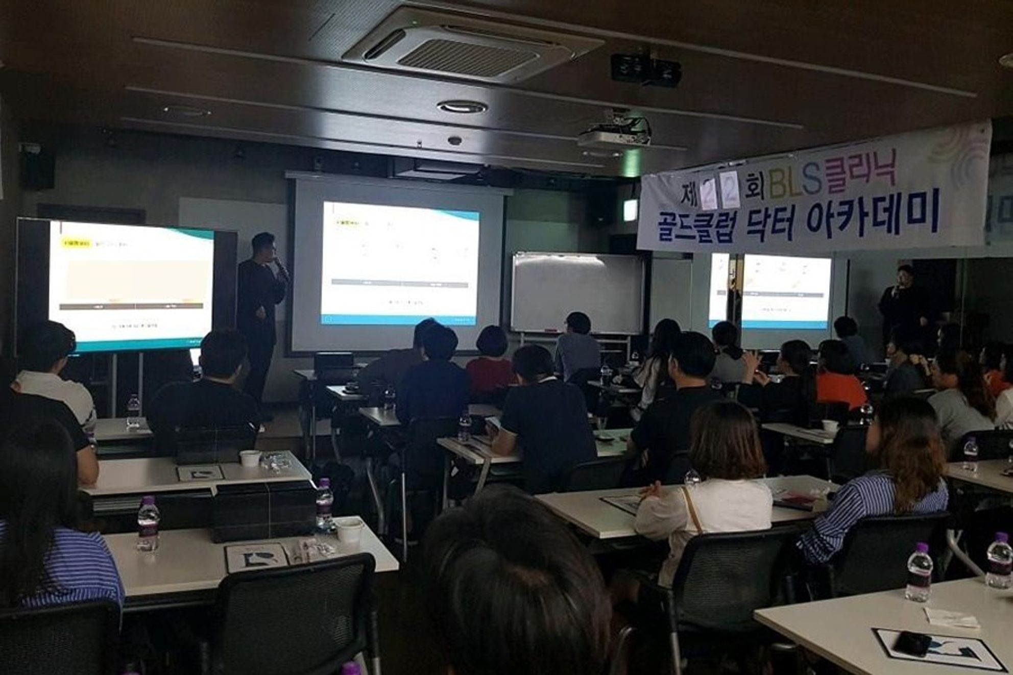 골드클럽 닥터 아카데미 현수막이 걸린 강의실에서 참석자들이 앞쪽 화면과 마이크를 든 사람을 바라보는 장면