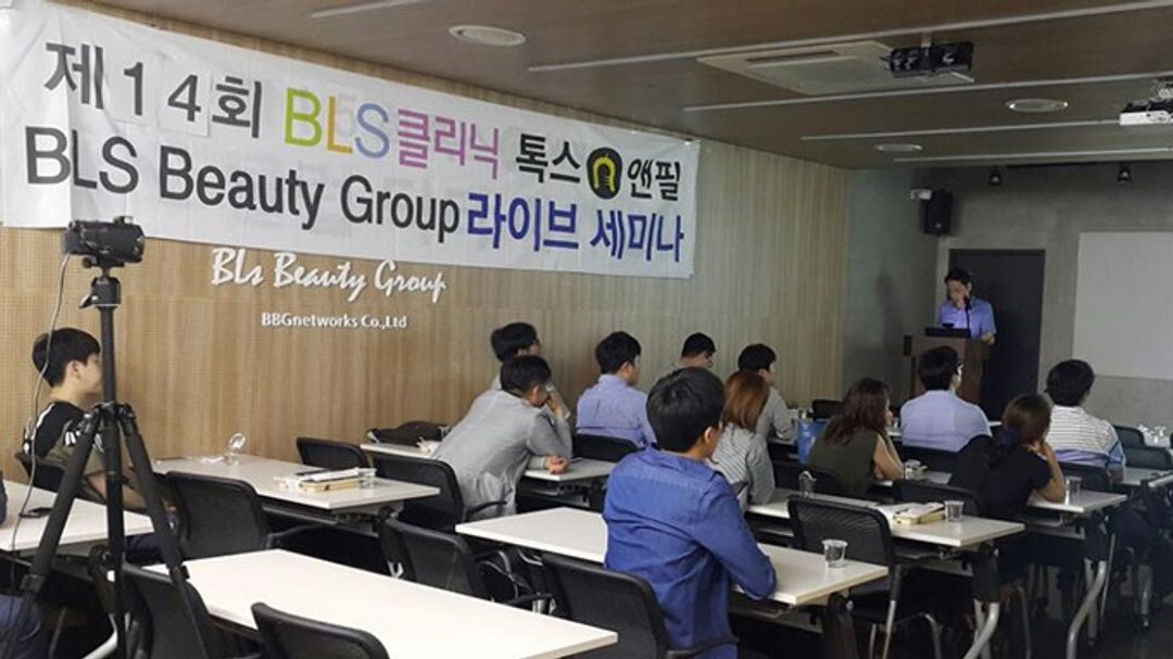 라이브 세미나 현수막이 걸린 강의실에서 참석자들이 책상 앞에 앉아 있고, 앞쪽 연단에 한 사람이 서 있는 모습