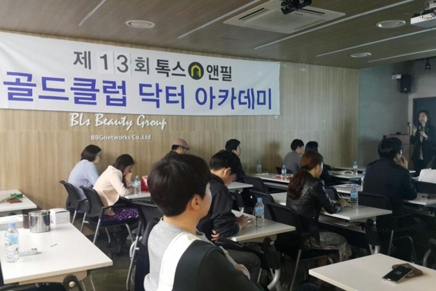톡스앤필 현수막이 걸린 나무 벽 아래 참석자들이 앉아 있고 오른쪽 앞에서 한 사람이 마이크를 들고 서 있는 모습