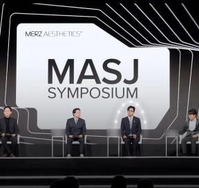 'MASJ SYMPOSIUM' 대형 화면 아래 무대에 네 사람이 의자에 앉아 있는 모습(명패 글자는 흐리게 처리)