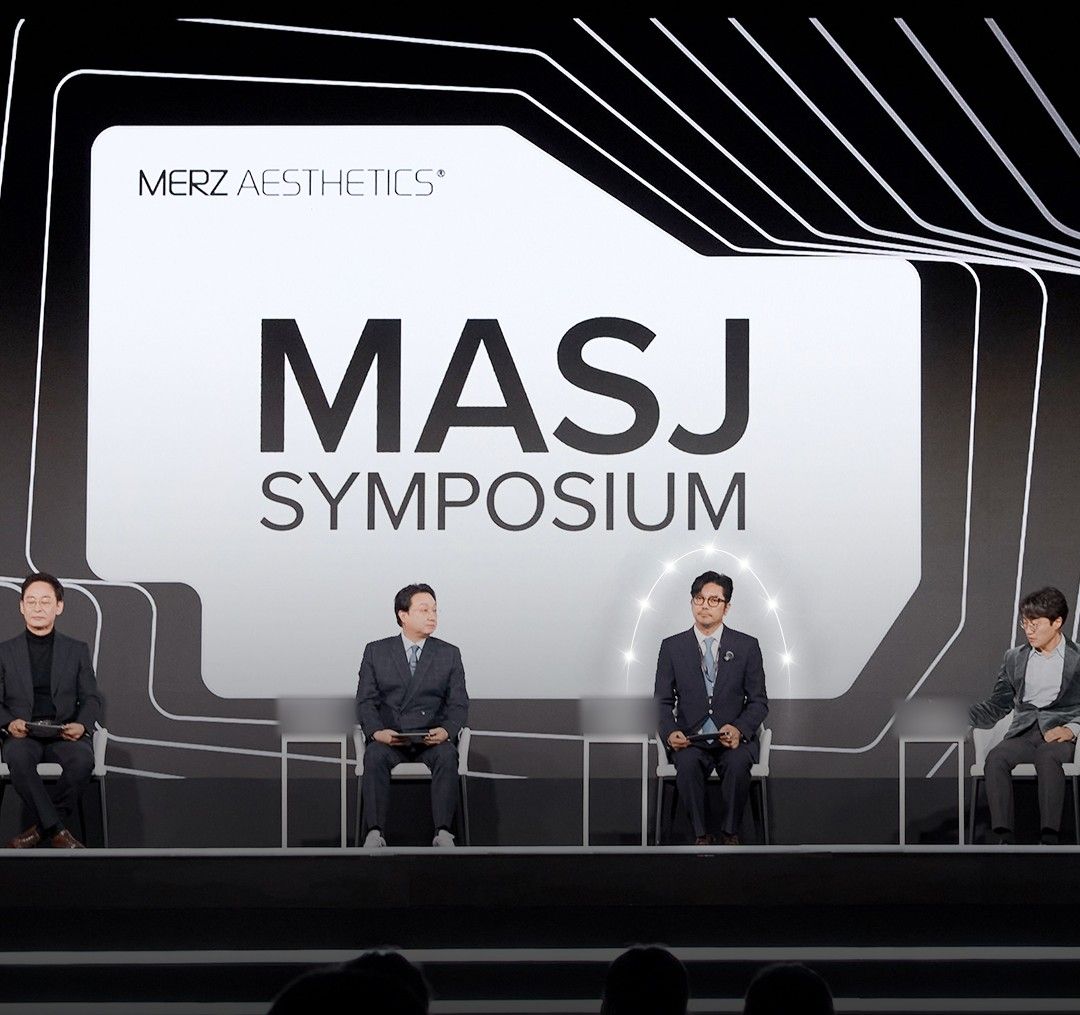 'MASJ SYMPOSIUM' 대형 화면 아래 무대에 네 사람이 의자에 앉아 있는 모습(명패 글자는 흐리게 처리)