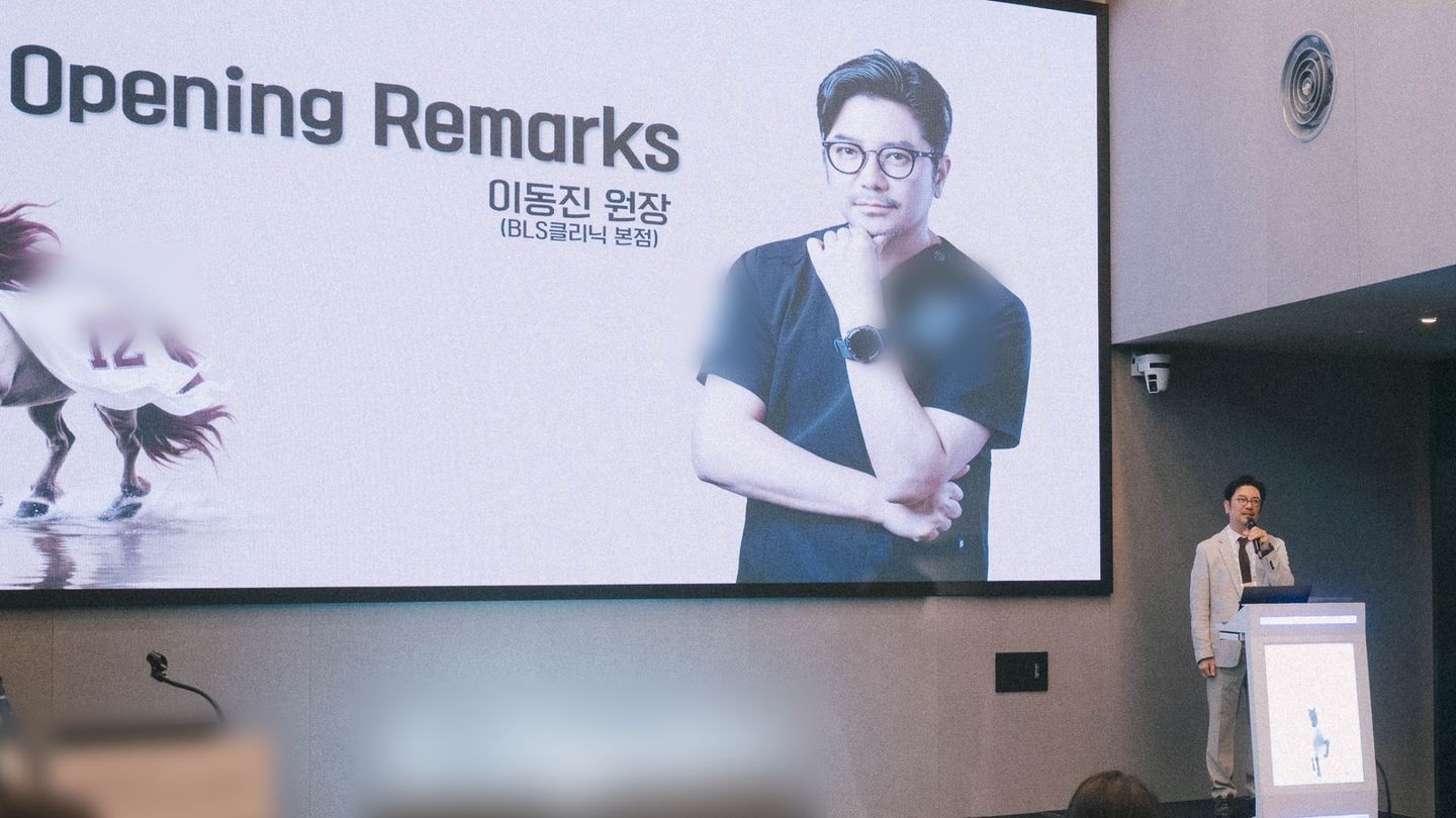 대형 화면에 'Opening Remarks'와 '이동진 원장(BLS클리닉 본점)' 소개 슬라이드가 띄워져 있고, 오른쪽 연단에서 이동진 원장이 마이크를 들고 말하고 있다