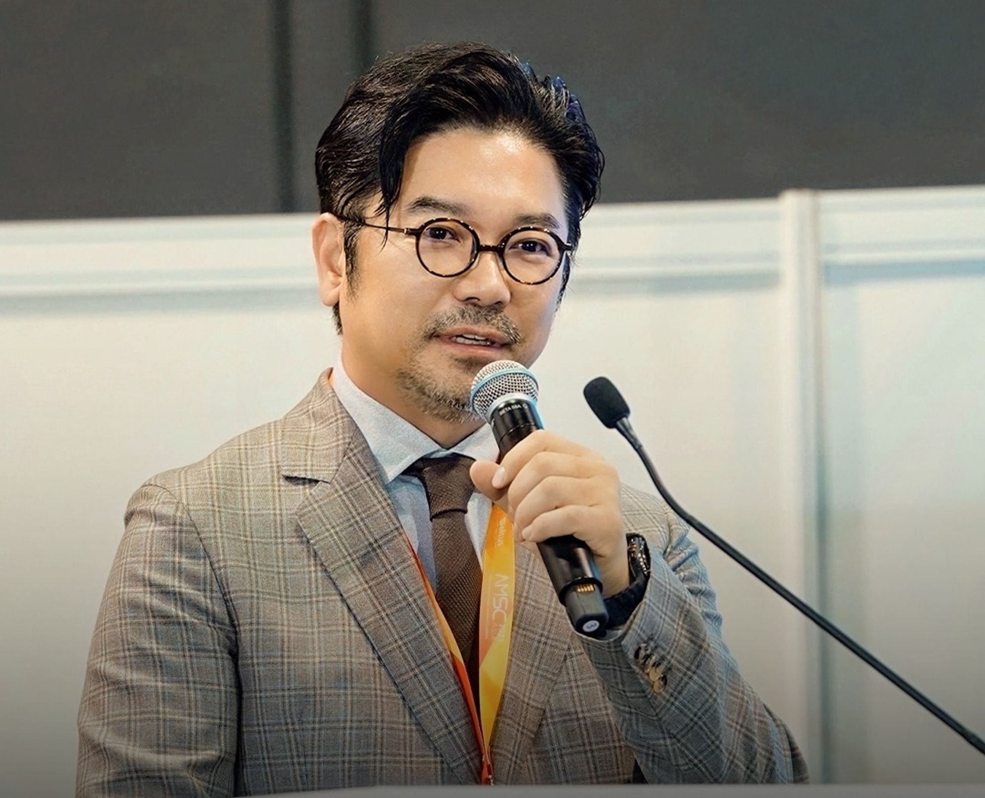 체크무늬 정장 차림의 한 사람이 마이크를 들고 강단에서 말하는 모습