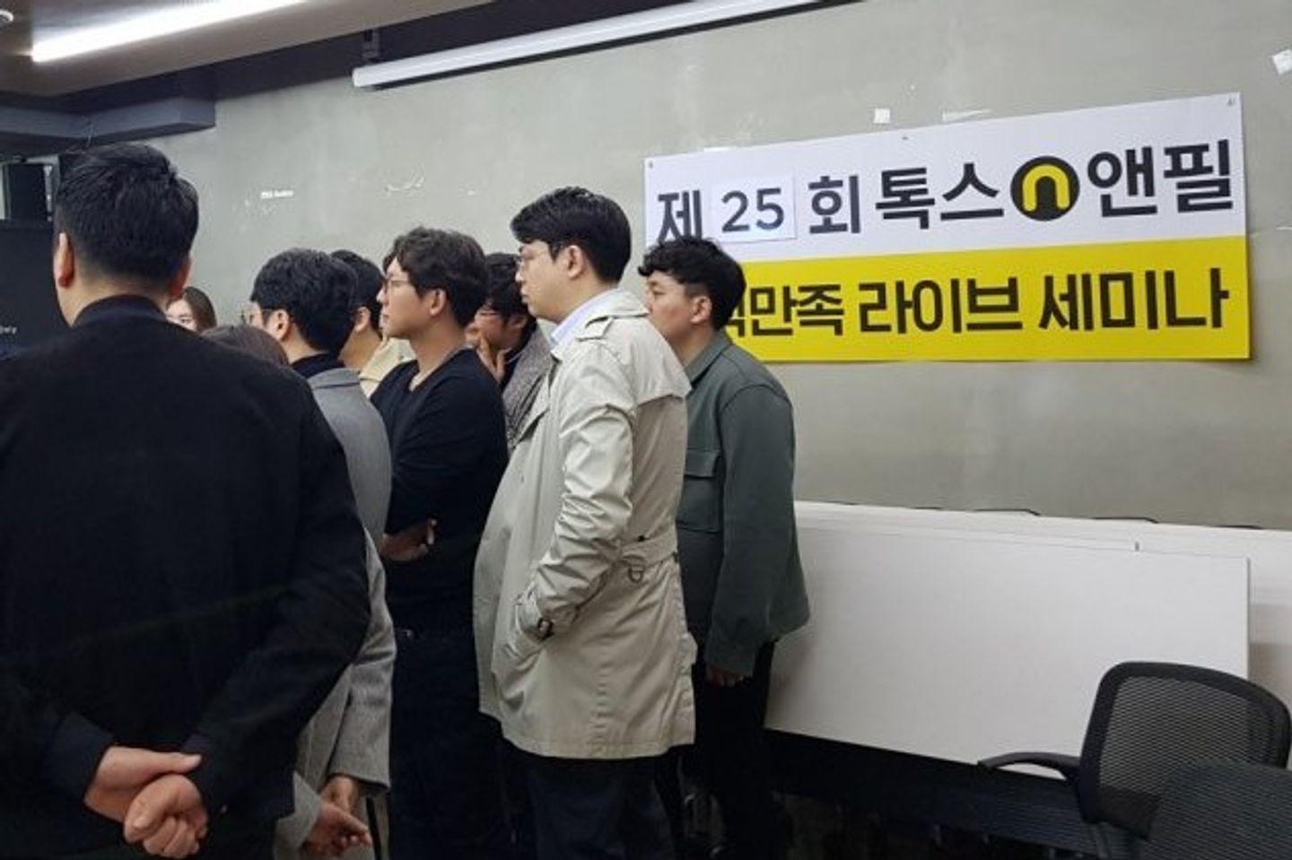 톡스앤필 라이브 세미나 현수막이 걸린 벽 앞에 참석자들이 모여 서서 한쪽을 지켜보는 모습