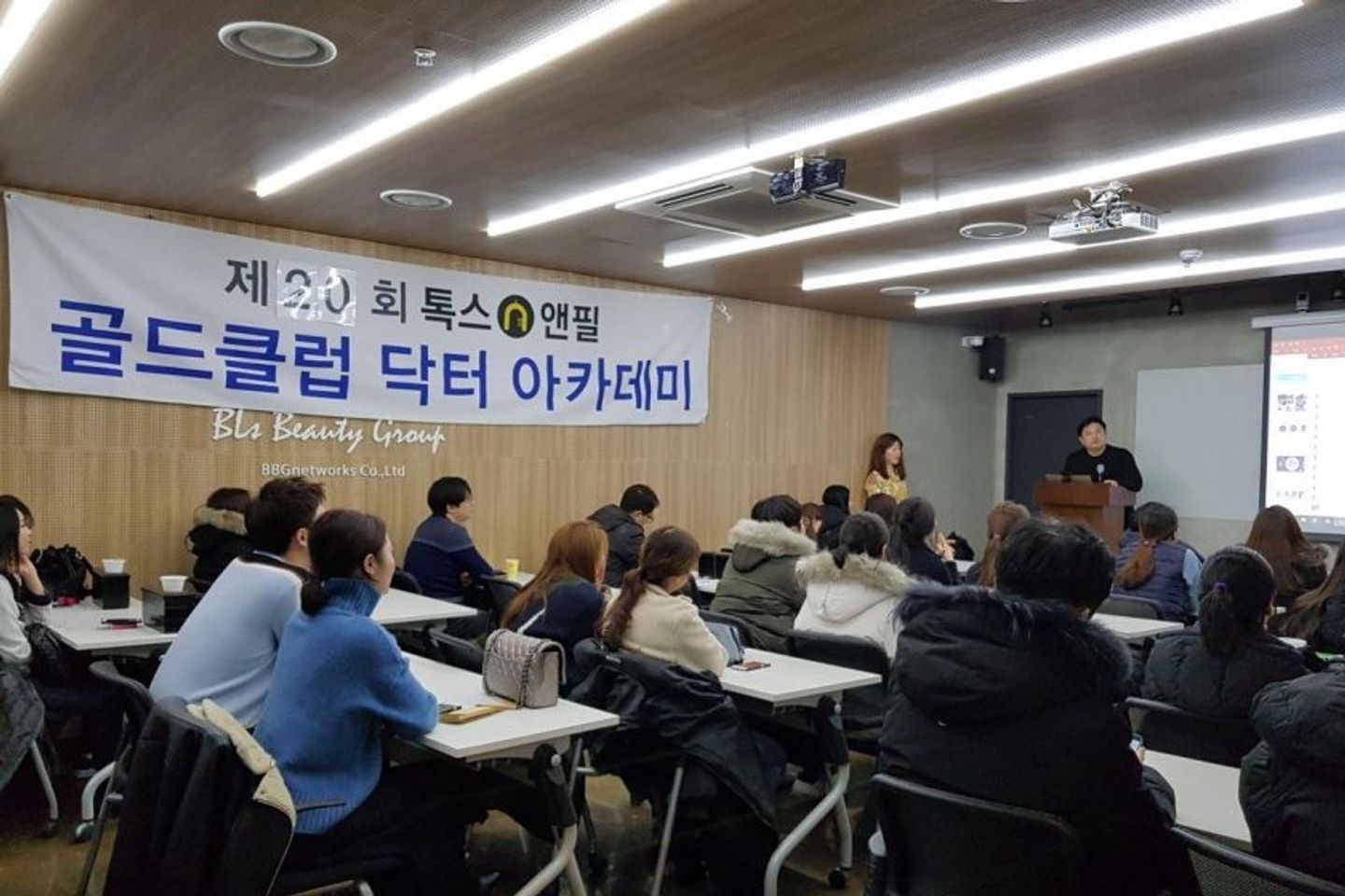 톡스앤필 현수막이 걸린 나무 벽 앞에 참석자들이 앉아 있고 앞쪽 연단에 한 사람이 서 있는 모습