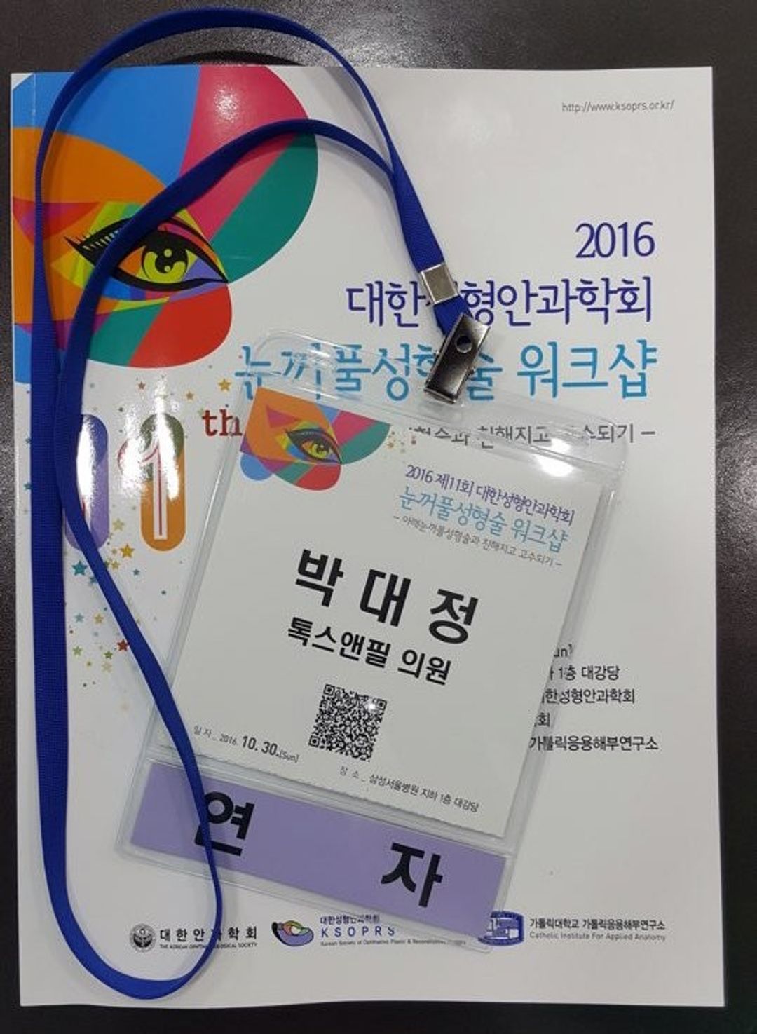 학술 워크샵 책자 표지 위에 파란 목걸이 줄이 달린 명찰이 놓인 모습