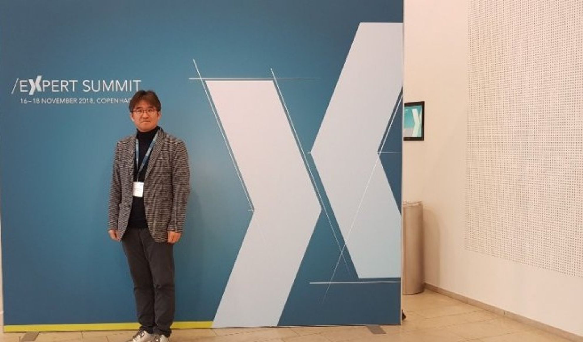 'EXPERT SUMMIT' 글자가 적힌 파란 배경막 앞에 한 사람이 서 있는 모습