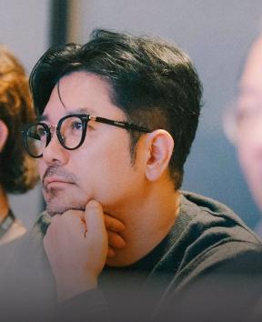 안경을 쓴 한 사람이 턱을 괴고 앞쪽을 바라보는 모습