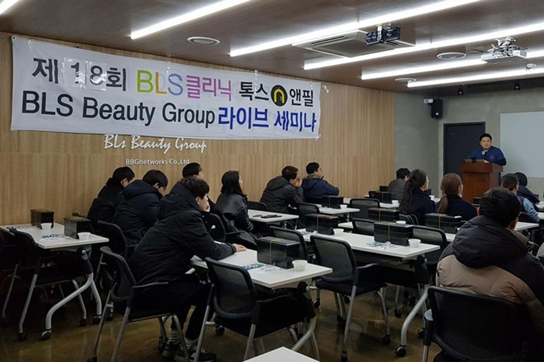 현수막이 걸린 세미나실에서 참석자들이 책상에 앉아 있고 앞쪽 연단에 한 사람이 서 있는 모습