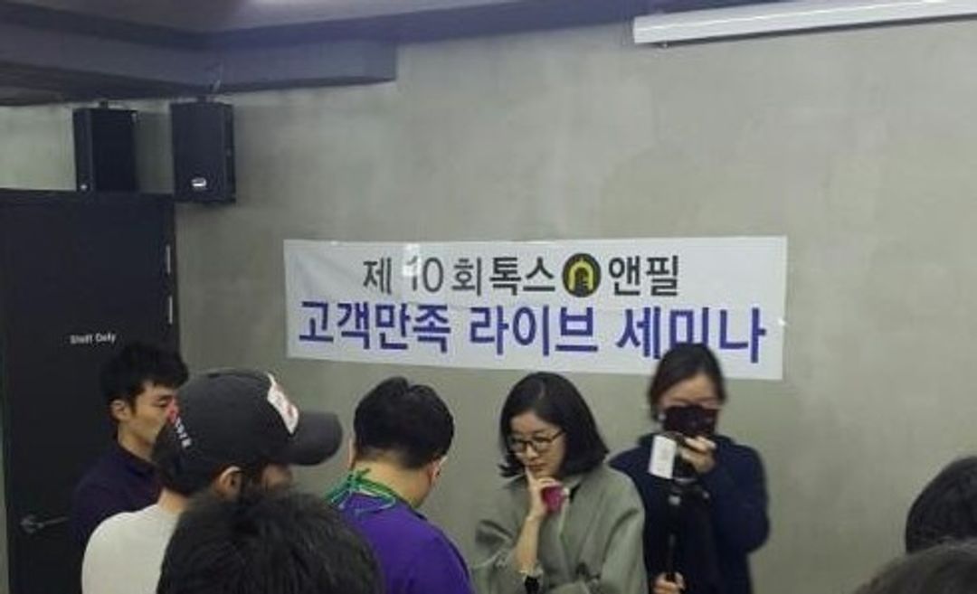 '제10회 톡스앤필 고객만족 라이브 세미나' 현수막이 걸린 방에 여러 사람이 서 있고 한 사람이 카메라로 촬영하는 모습