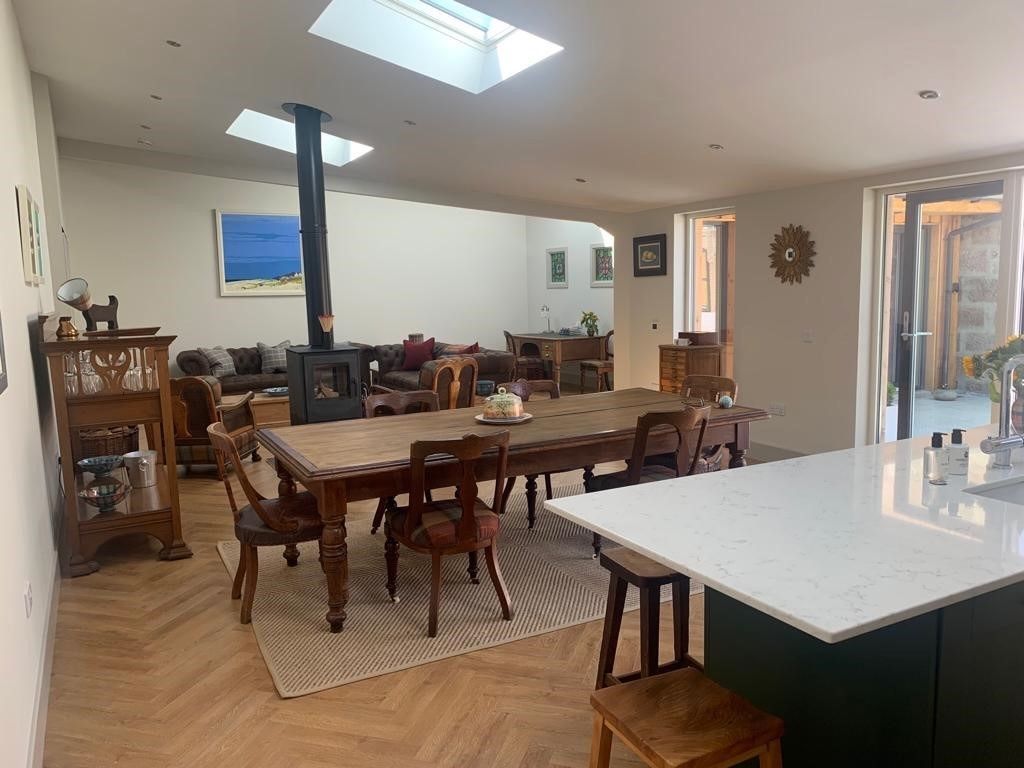 A kitchen diner with a wood burning stove, long wooden dining table, and a three-piece suite.