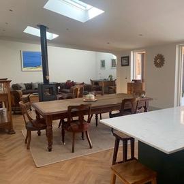 A kitchen diner with a wood burning stove, long wooden dining table, and a three-piece suite.