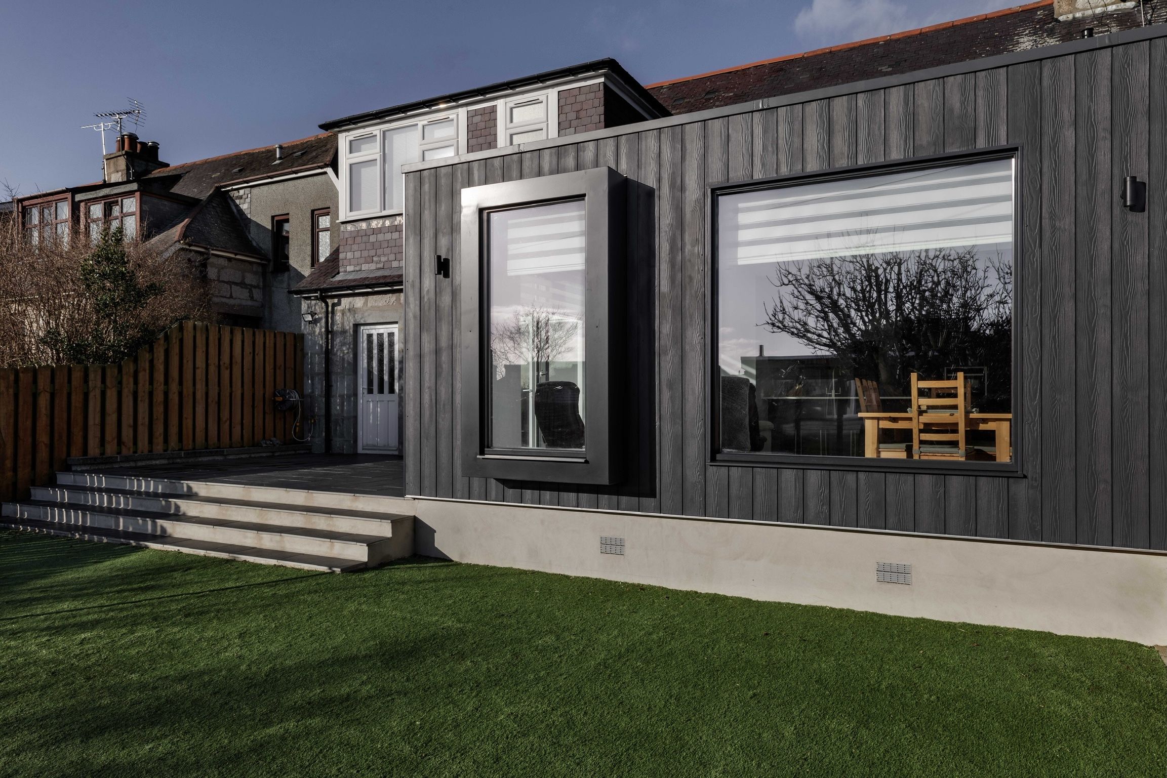 View is from the rear of the property. It shows a modern extension with dark wood cladding and large windows.