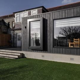 View is from the rear of the property. It shows a modern extension with dark wood cladding and large windows.